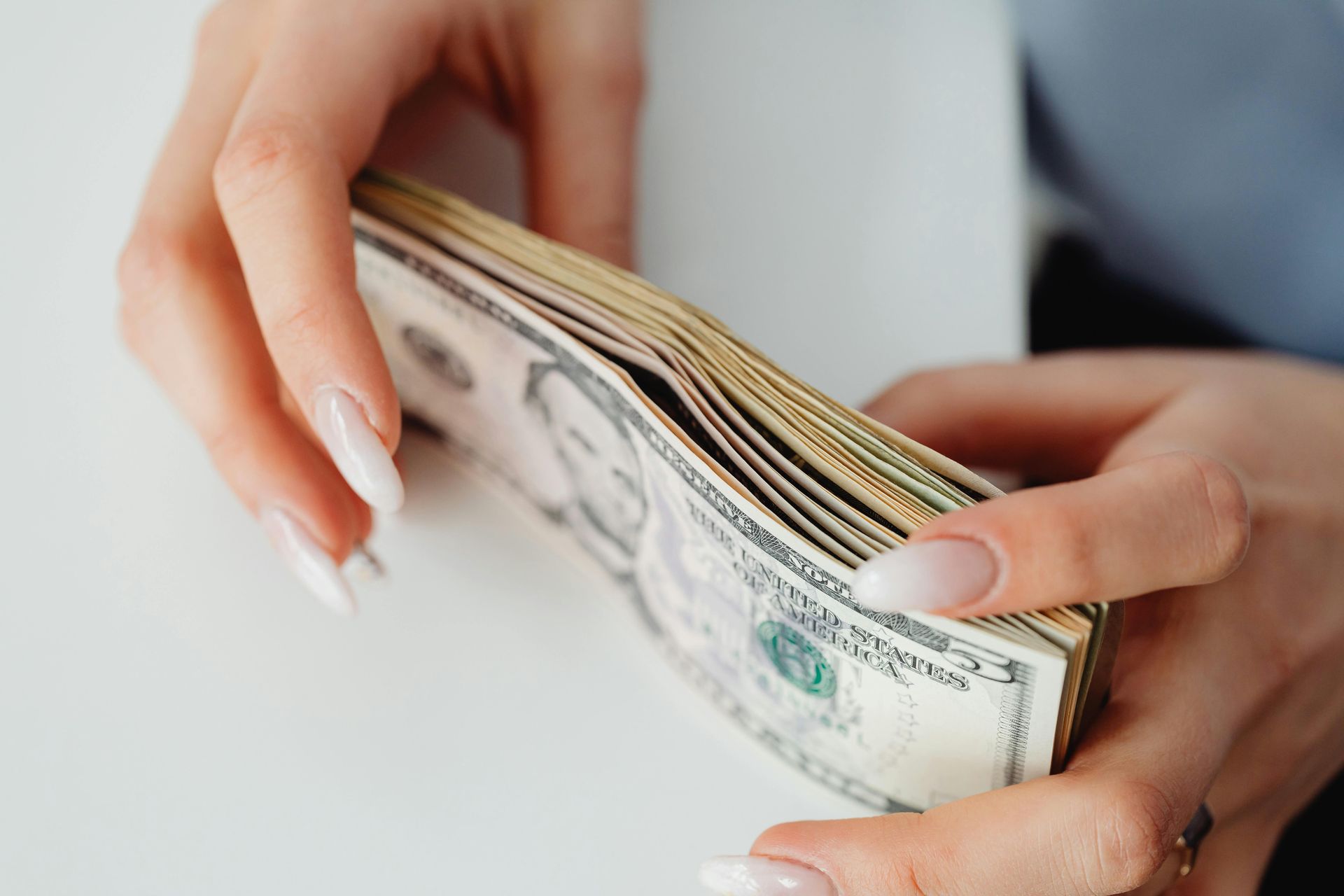 Hands counting a stack of U.S. dollar bills on a white surface