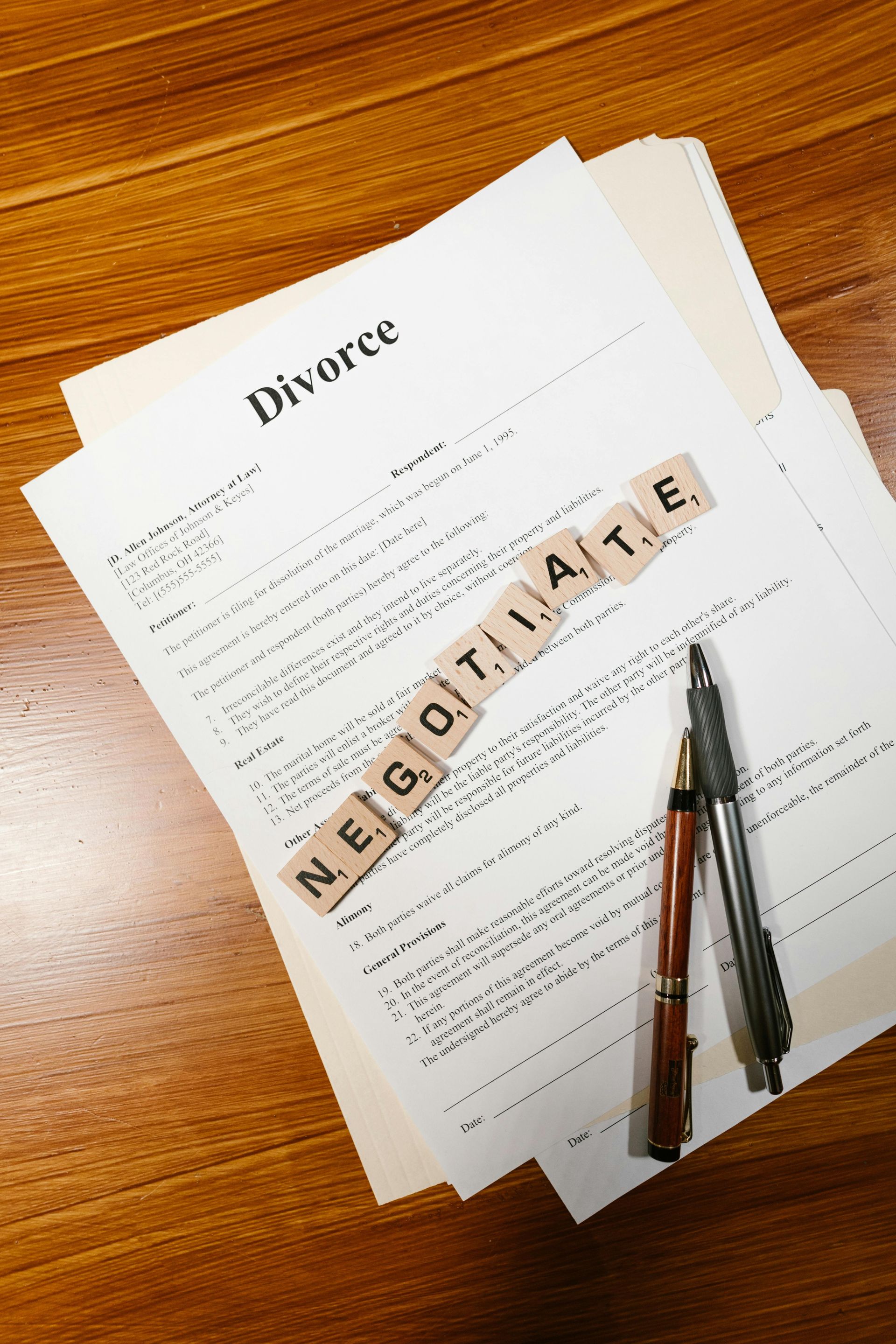 Divorce documents on a wooden table, with a “NEGOTIATOR” letter tile and pen on top