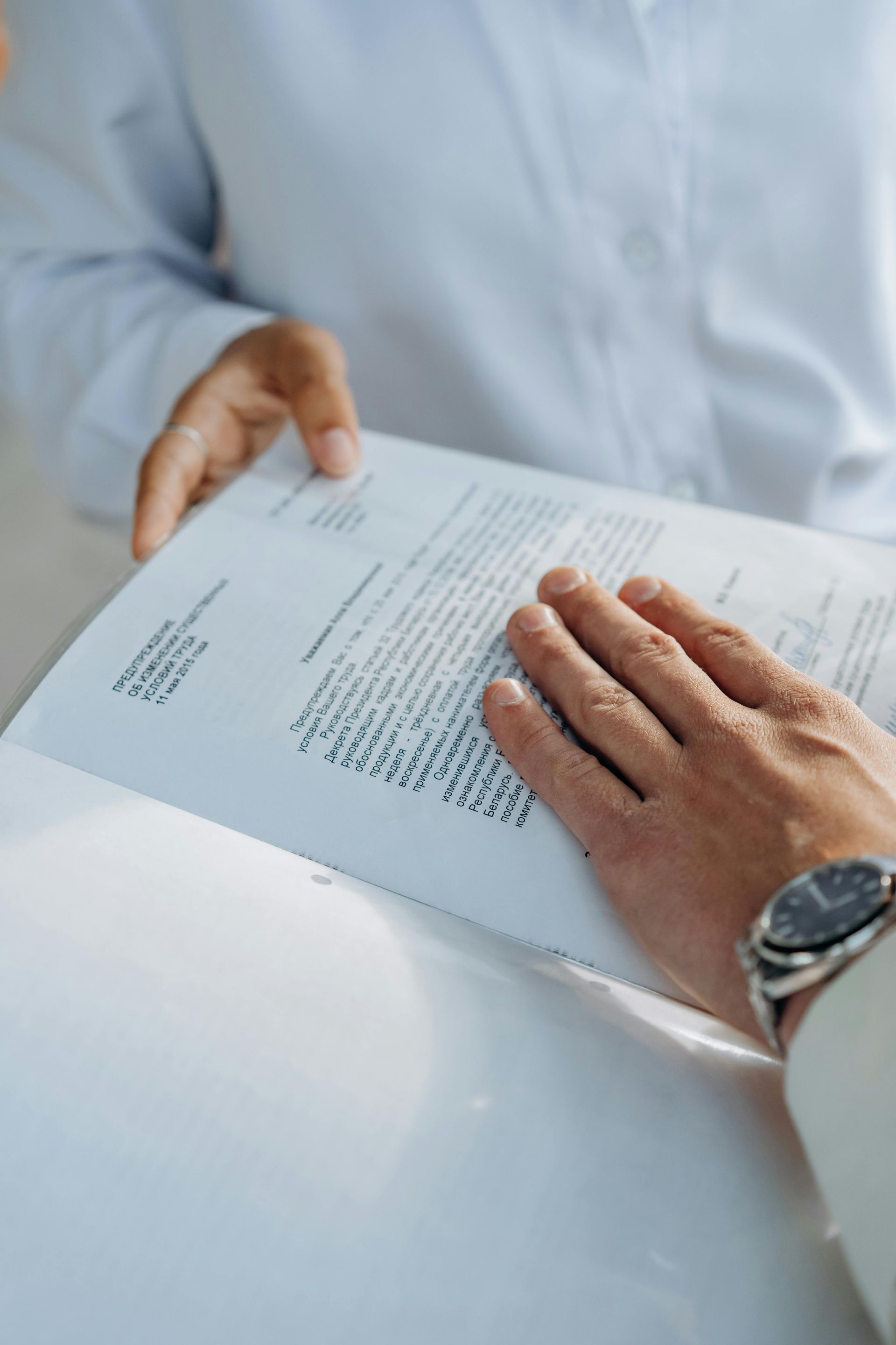Hands reviewing a document on a white table, with a wristwatch visible.