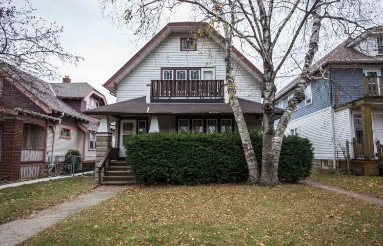 A white kenosha house with a balcony and a tree in front of it.
