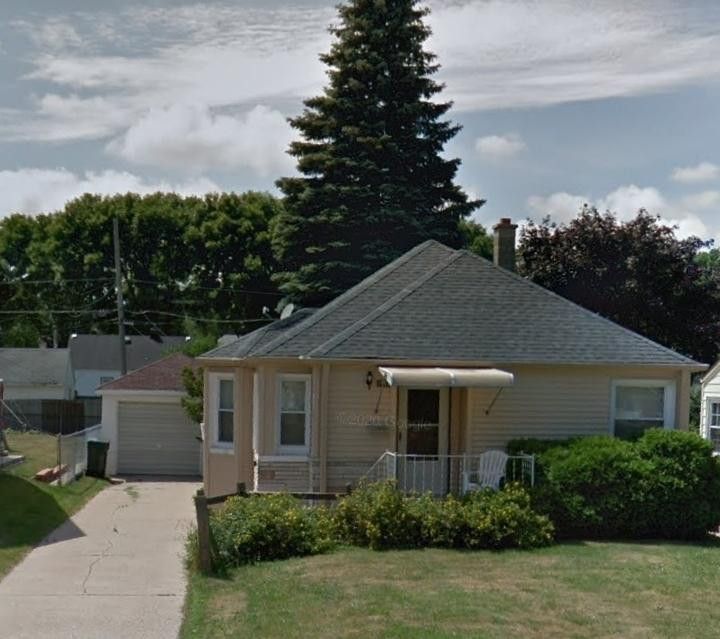 A small wauwatosa house with a gray roof is surrounded by trees