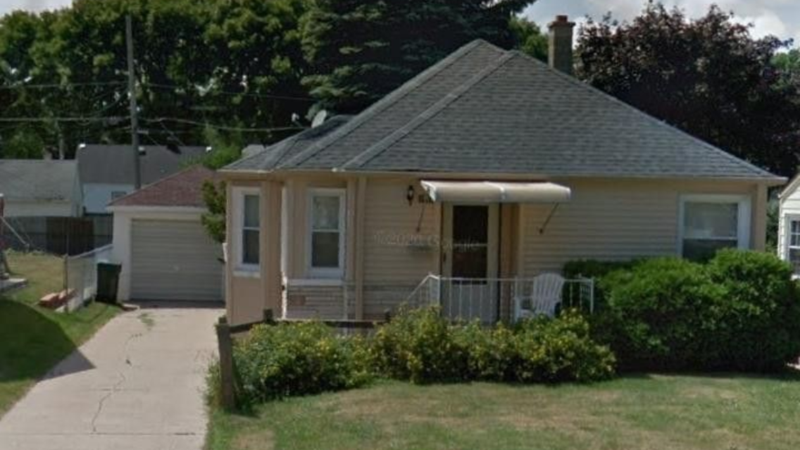 A light yellow, one-story suburban house with a dark gray shingled roof, a front porch, and an attached side garage.