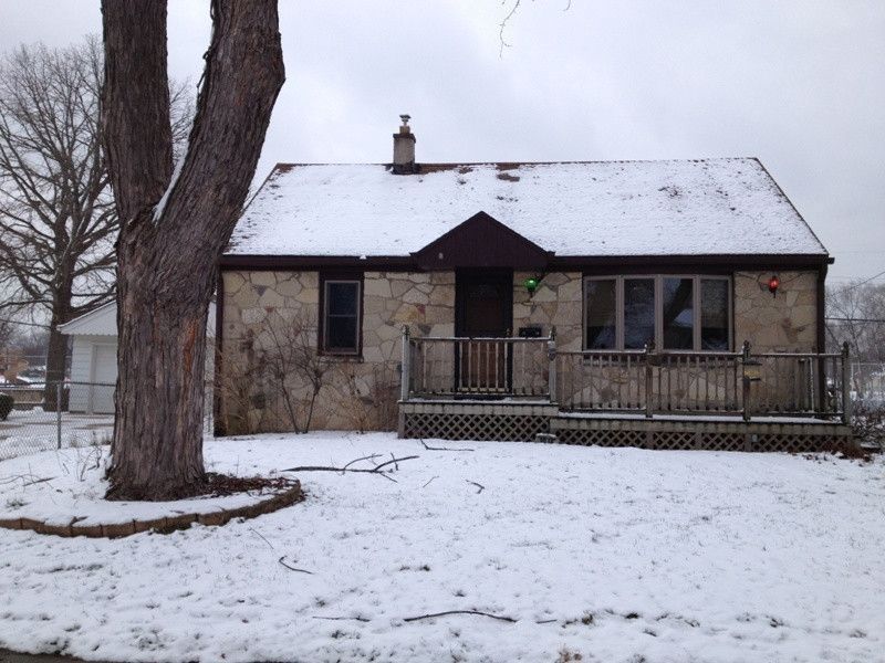 A brick house is surrounded by snow and trees.