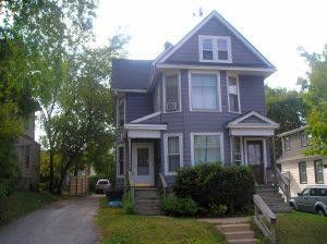 A large purple west allis house with a white roof is sitting on top of a lush green hill.