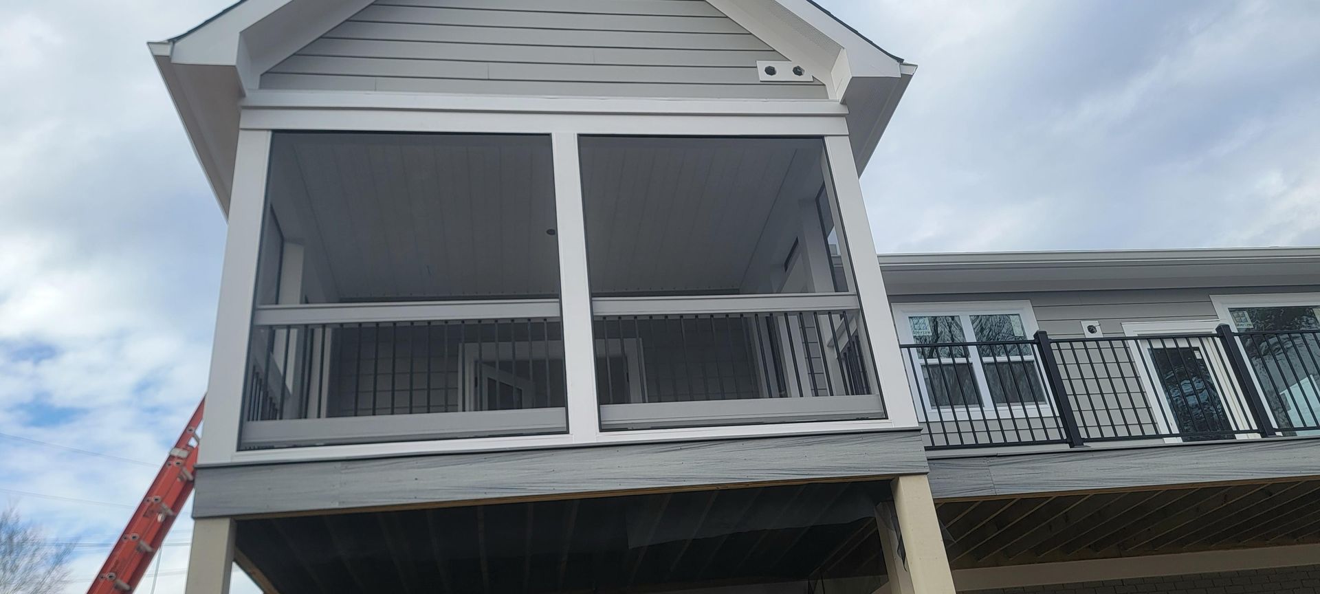 Two-story house with screened porch and white siding under a cloudy sky