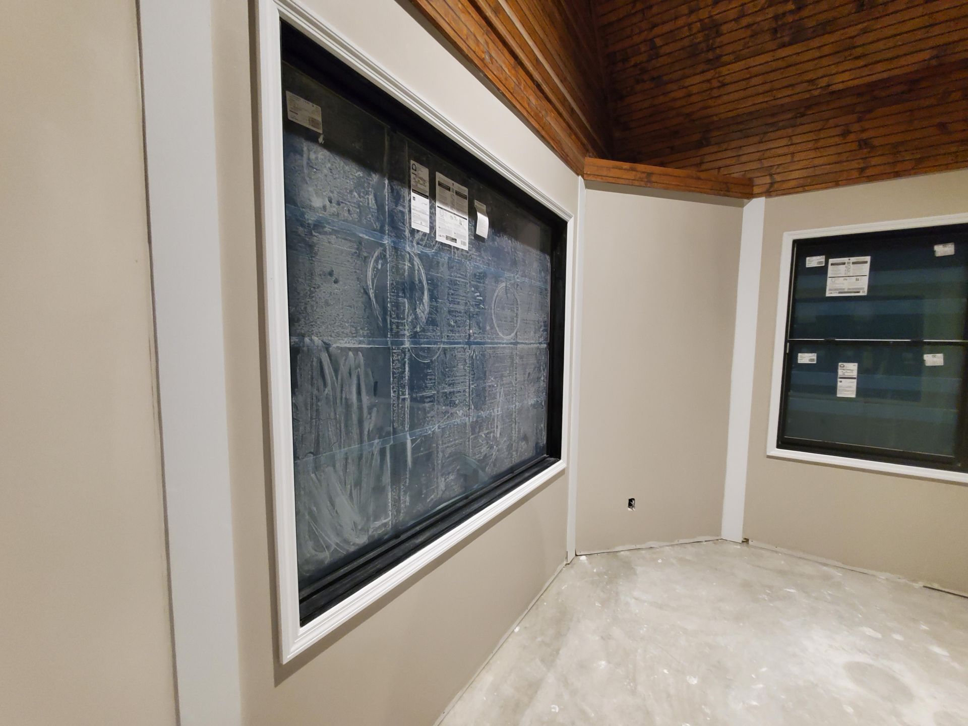Interior room with dark-framed windows, white walls, wood ceiling, and a floor covered in plastic sheeting