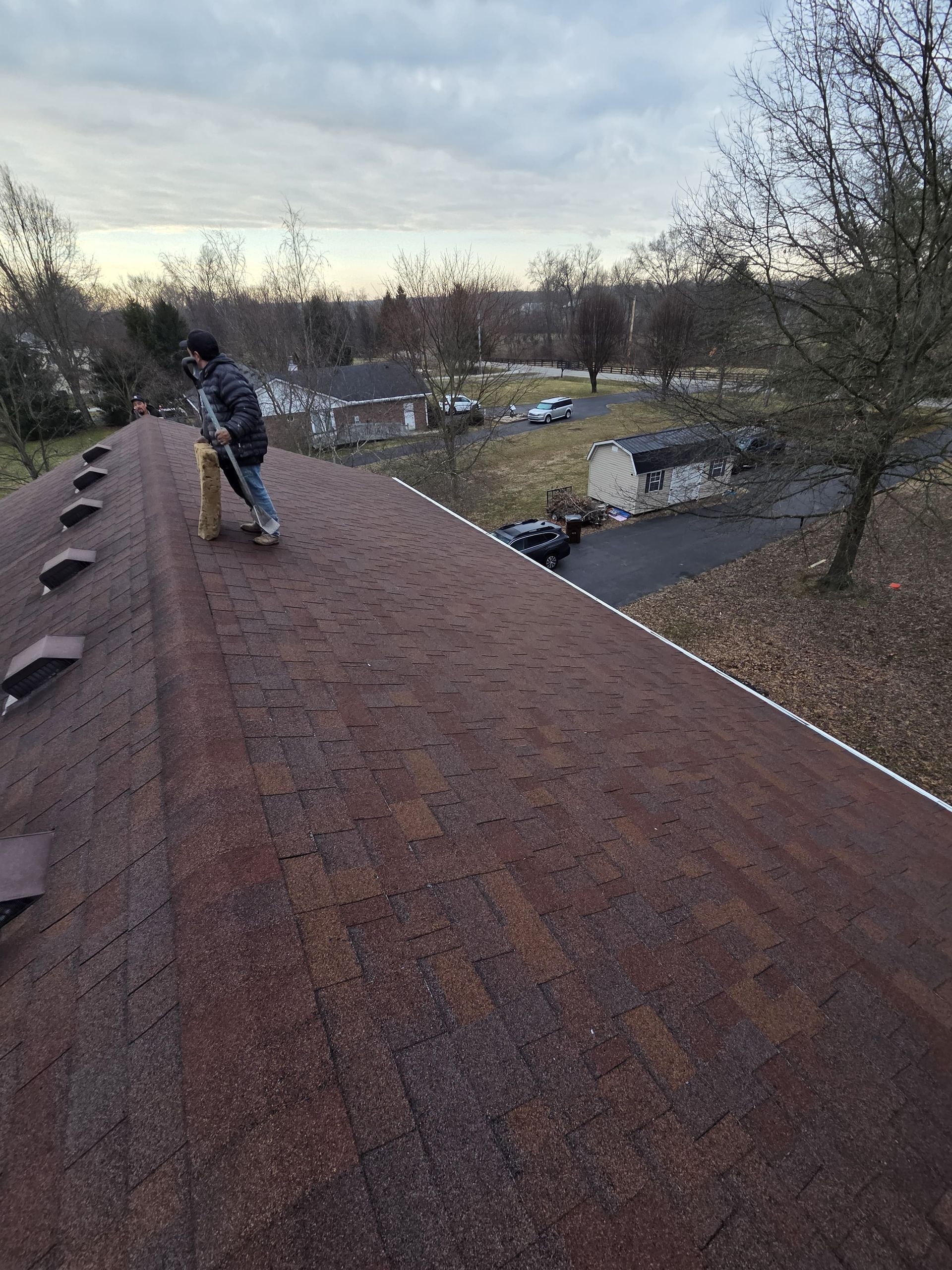 Person on a red shingled roof overlooking a creek and trees at dusk