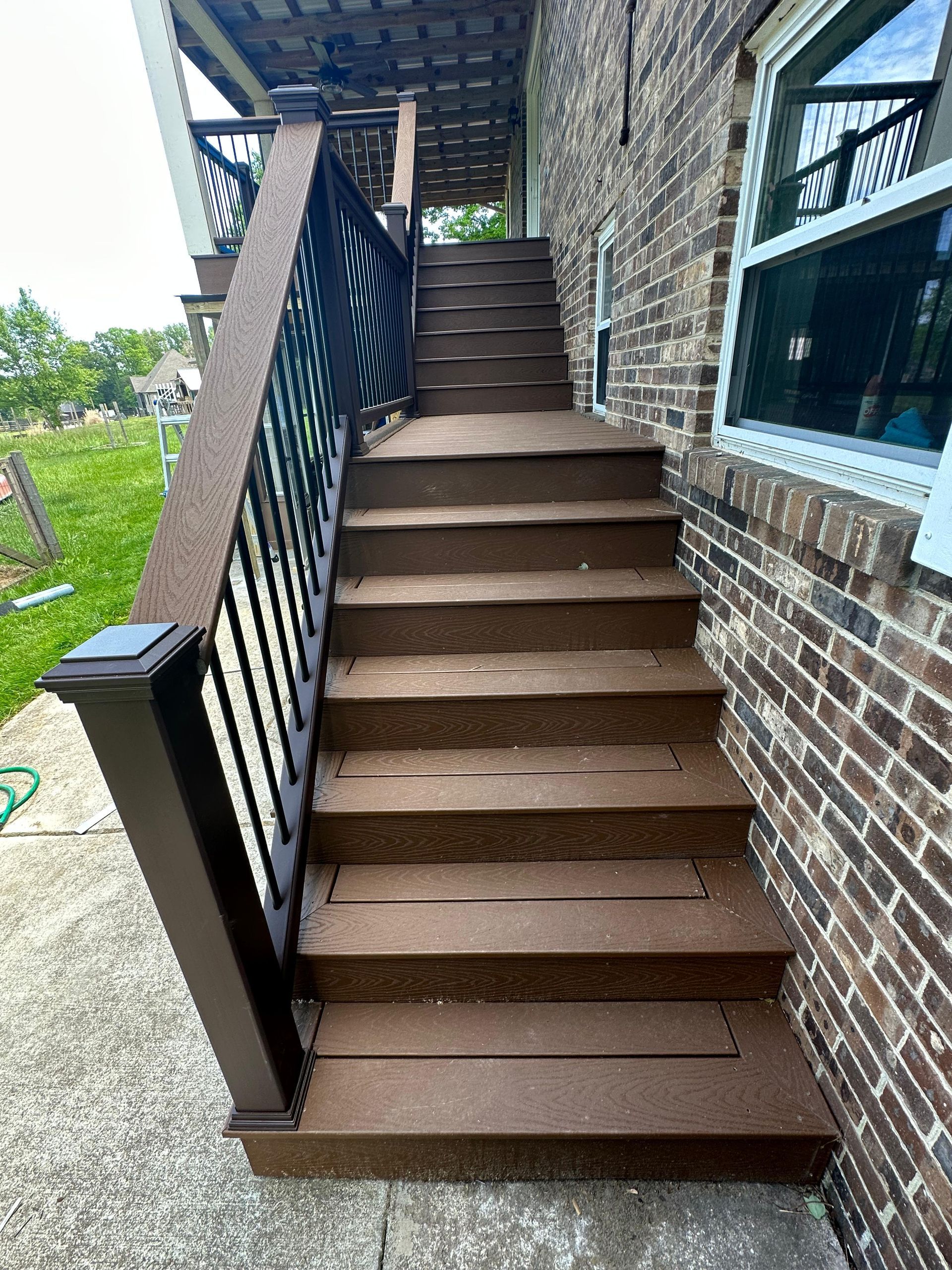 Outdoor brown stairs with black railing beside a stone house and windows