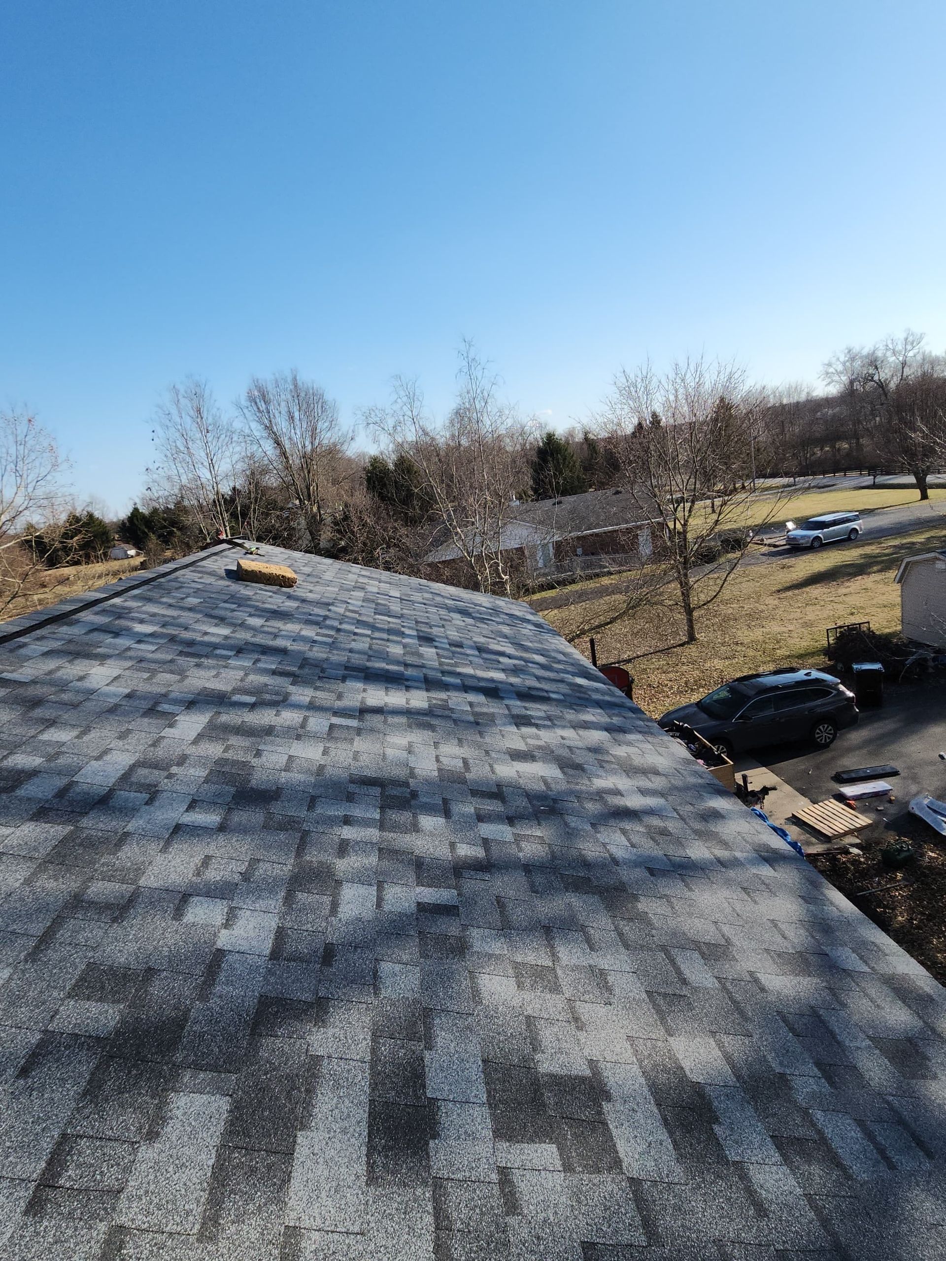 Shingled rooftop overlooking parked cars and bare trees under a clear blue sky