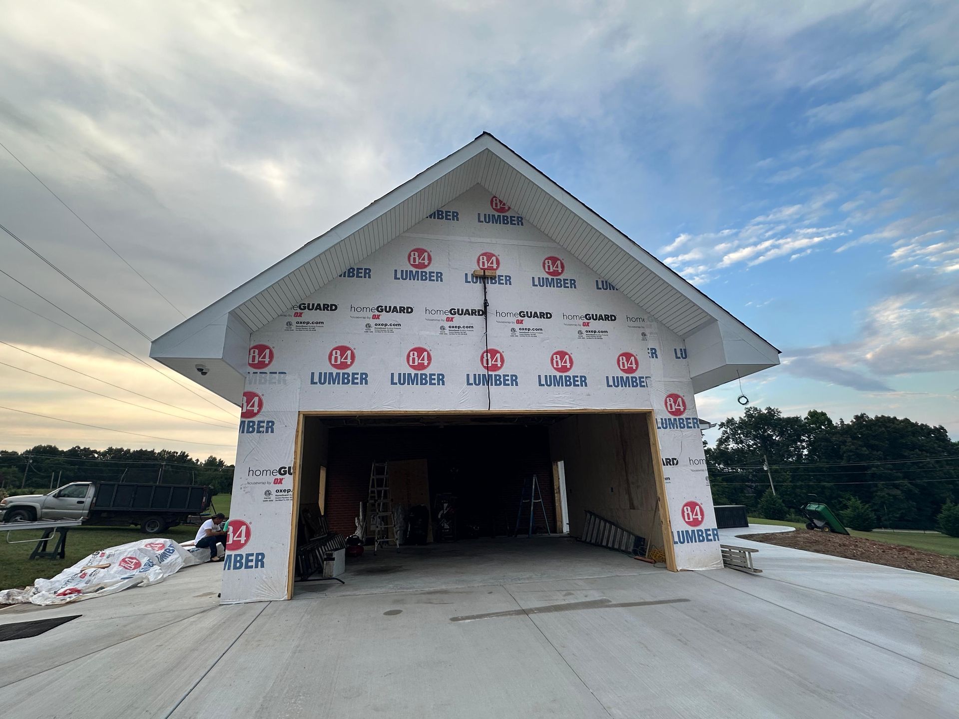 Partially built house with white wrap and an open garage, seen from the driveway under a cloudy sky