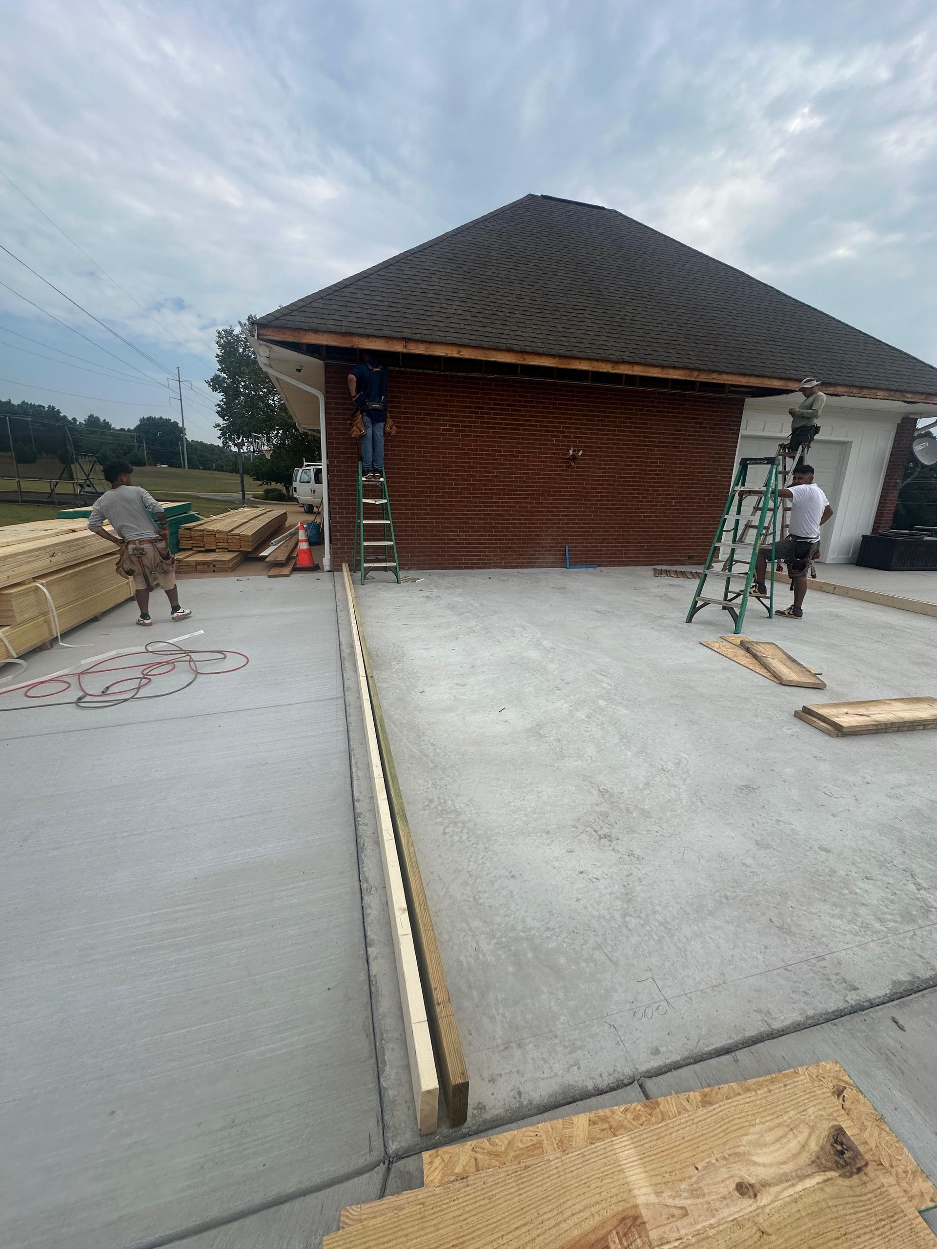 Workers on a rooftop pouring concrete beside a brick structure and ladder