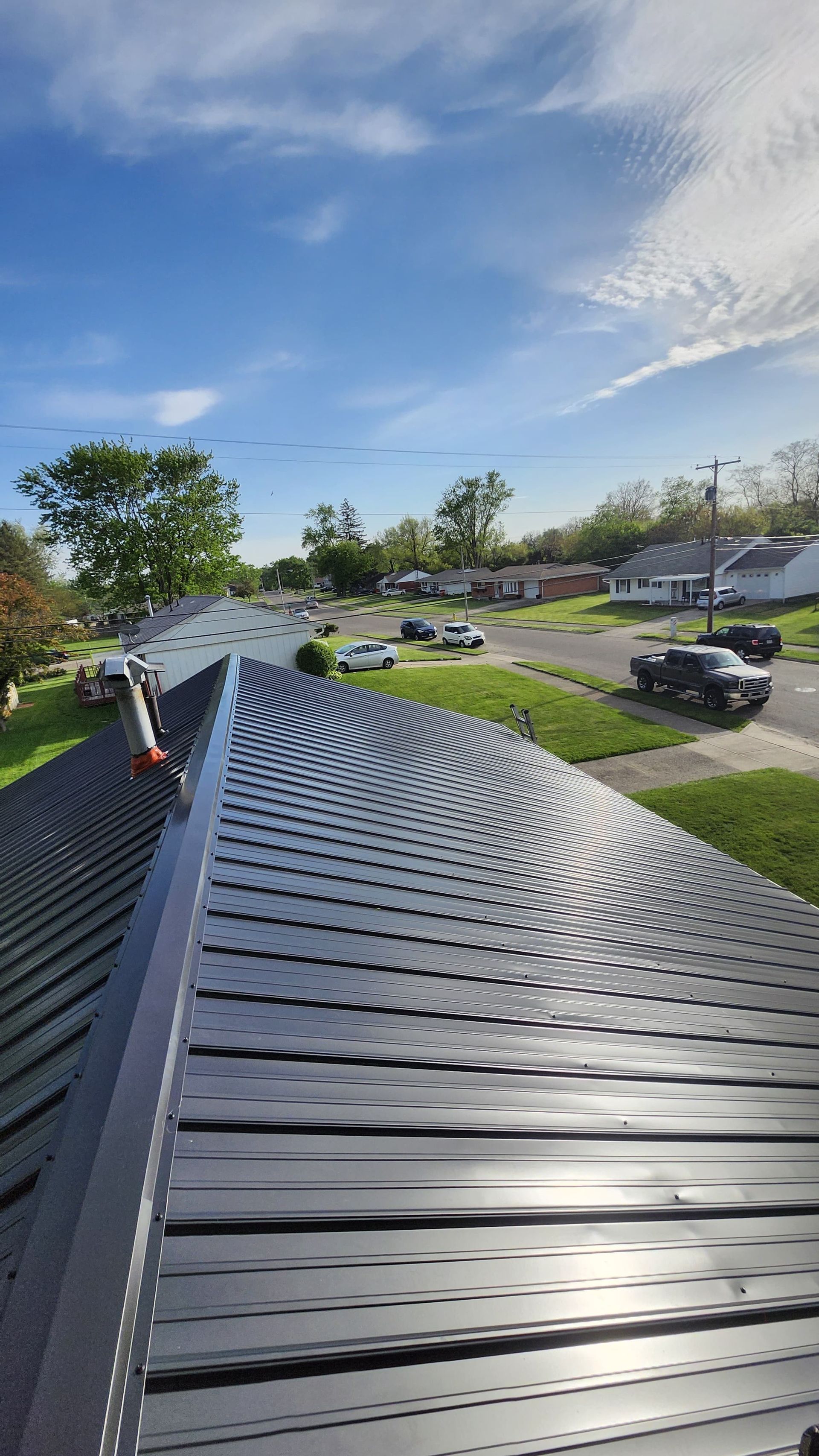 Black corrugated roof with workers, overlooking a green suburban street under a blue sky