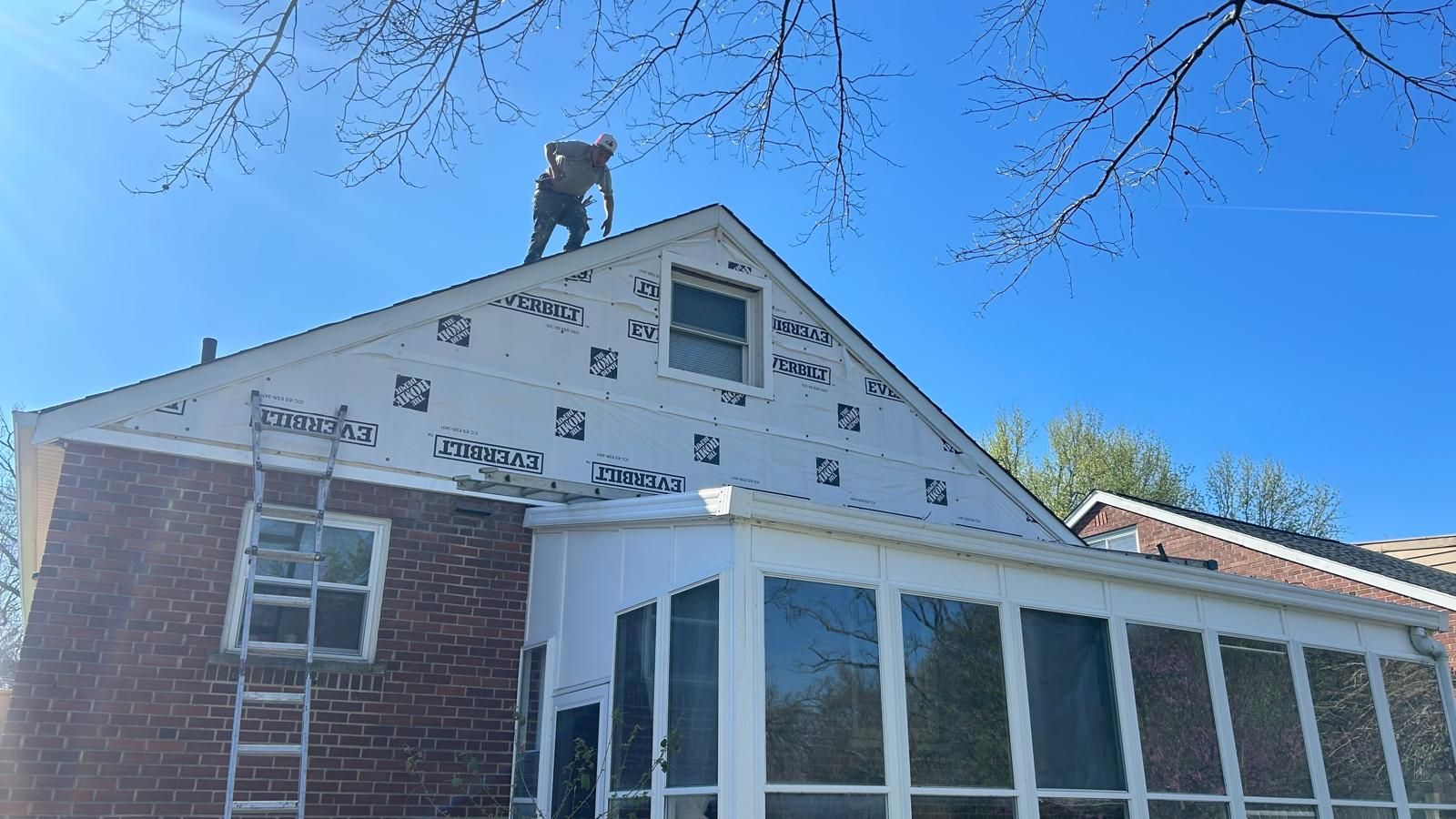 Two workers on a house roof during siding repair under a clear blue sky