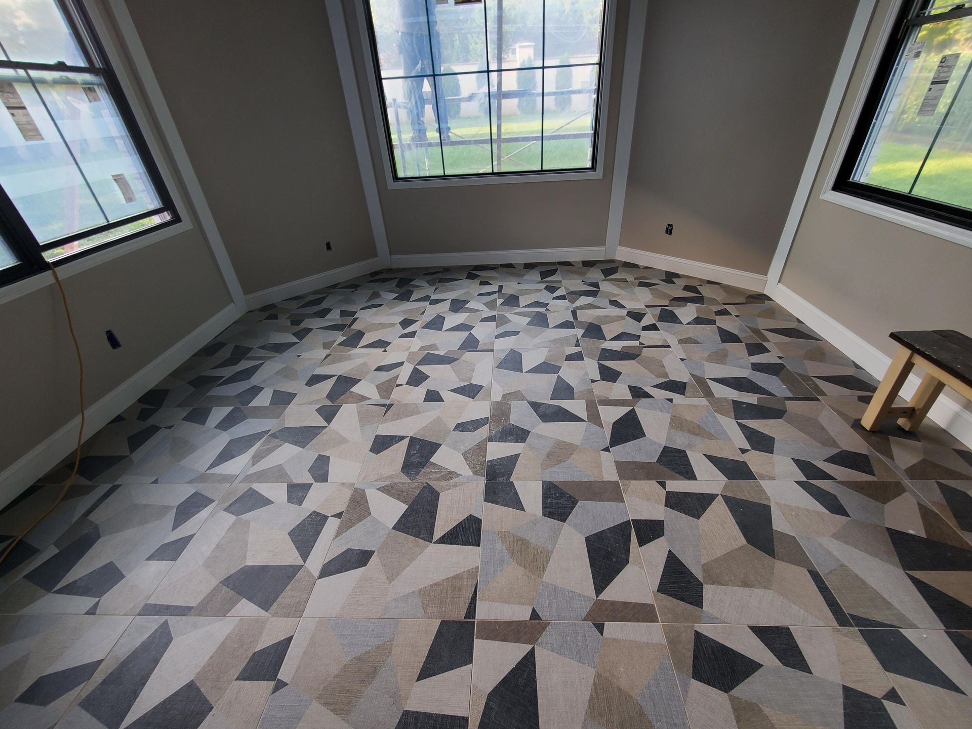 Empty room with gray geometric carpet, large windows, and a small wooden stool in the corner