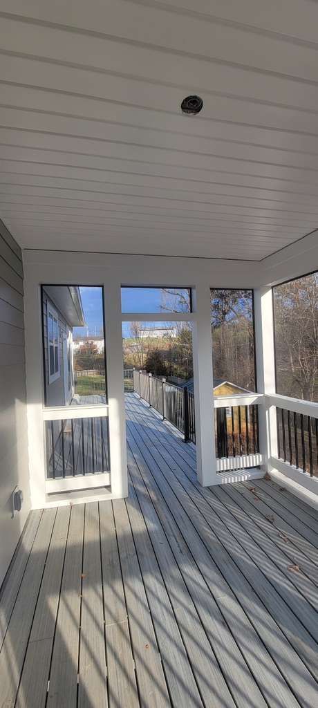 Sunlit porch with white railing, ceiling, and striped floor, overlooking trees and a distant house