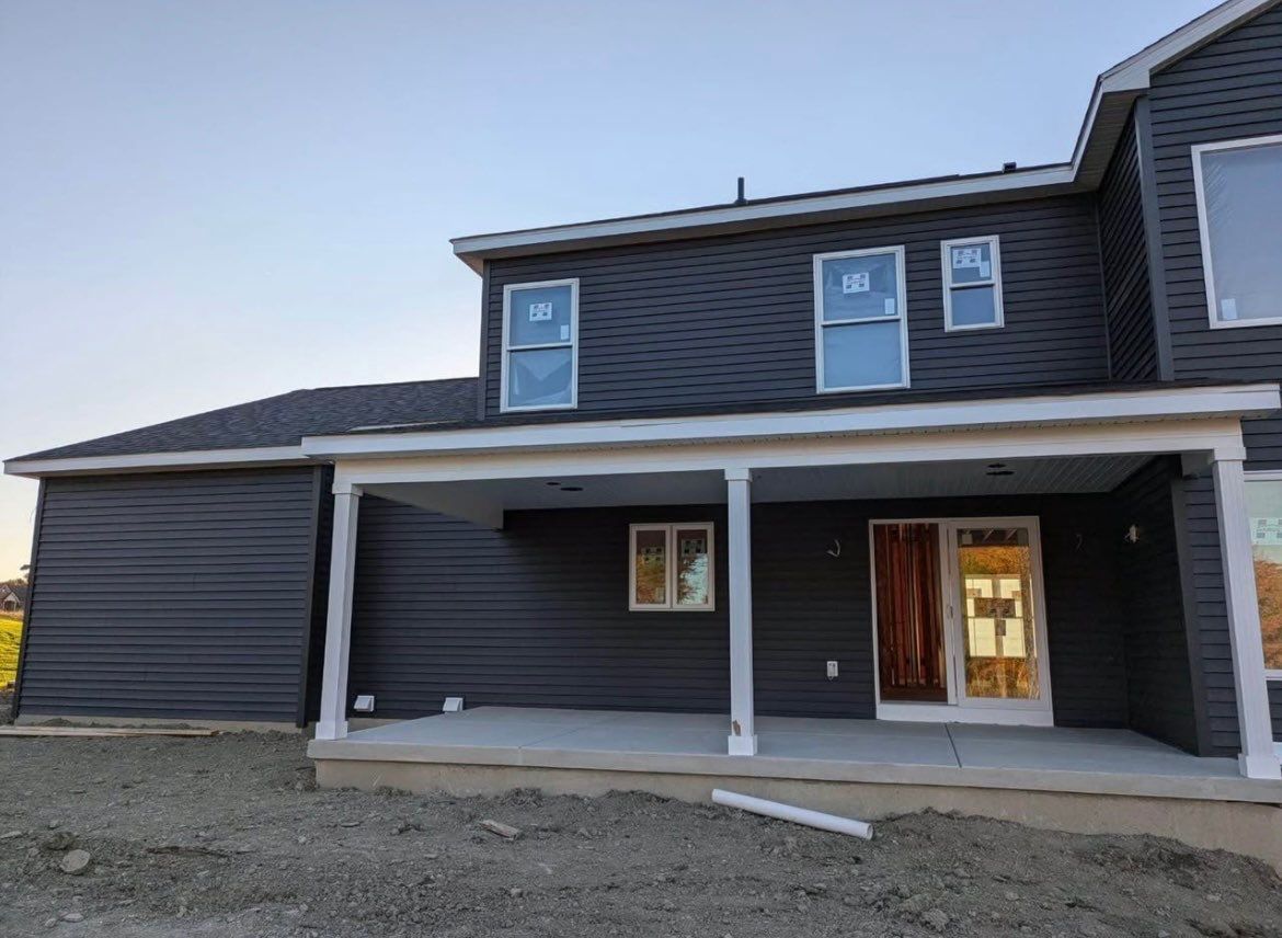 Dark gray two-story house exterior with a covered front porch and white trim under construction