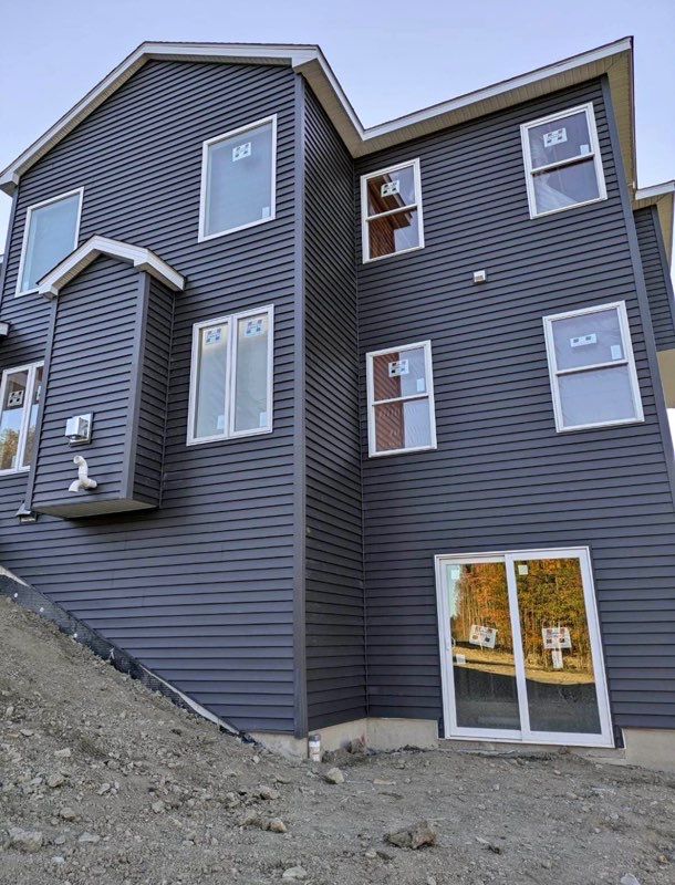 Gray multi-story townhouse exterior on a rocky slope, with white-trimmed windows and a glass patio door.