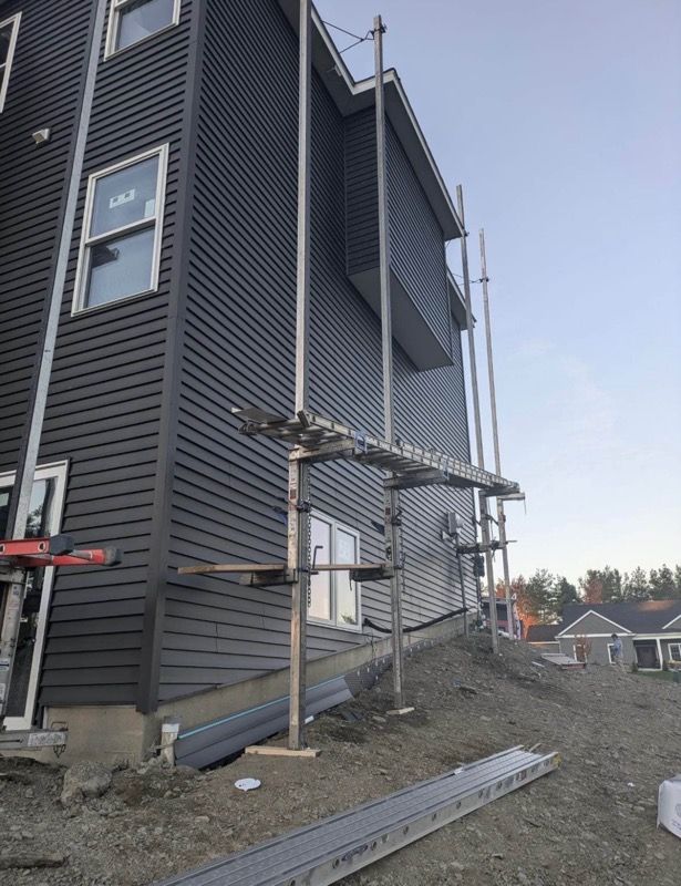 Gray house exterior with scaffolding beside a gravel yard under construction