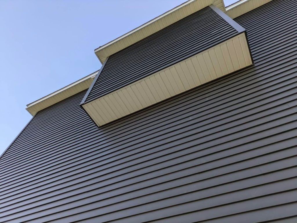 Low-angle view of a building facade with dark horizontal siding and two balcony overhangs against a blue sky