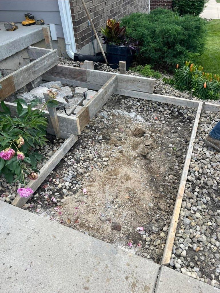 Rock-lined garden trench beside a house, bordered by concrete steps and lush greenery.