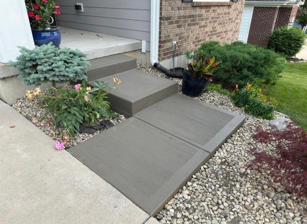 Front porch with gray concrete steps and ramp, bordered by flower beds and gravel landscaping.