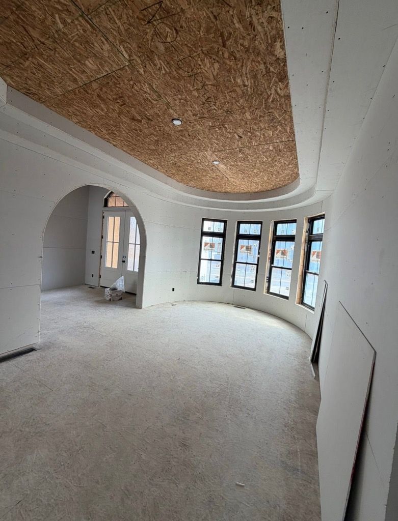 Curved unfinished interior with white walls, arched openings, and large windows under a wood-paneled ceiling.