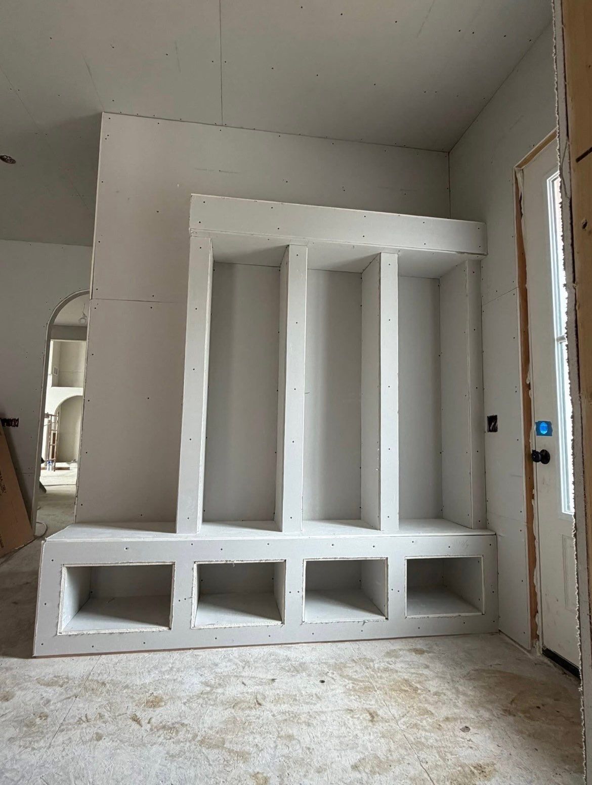 Built-in white shelving unit in an unfinished room with a window and doorway
