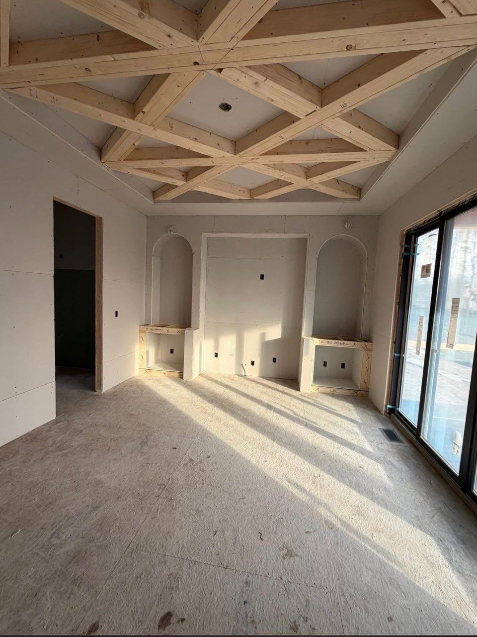 Bright empty room with geometric wood ceiling, built-in cabinets, and large glass doors on the right.