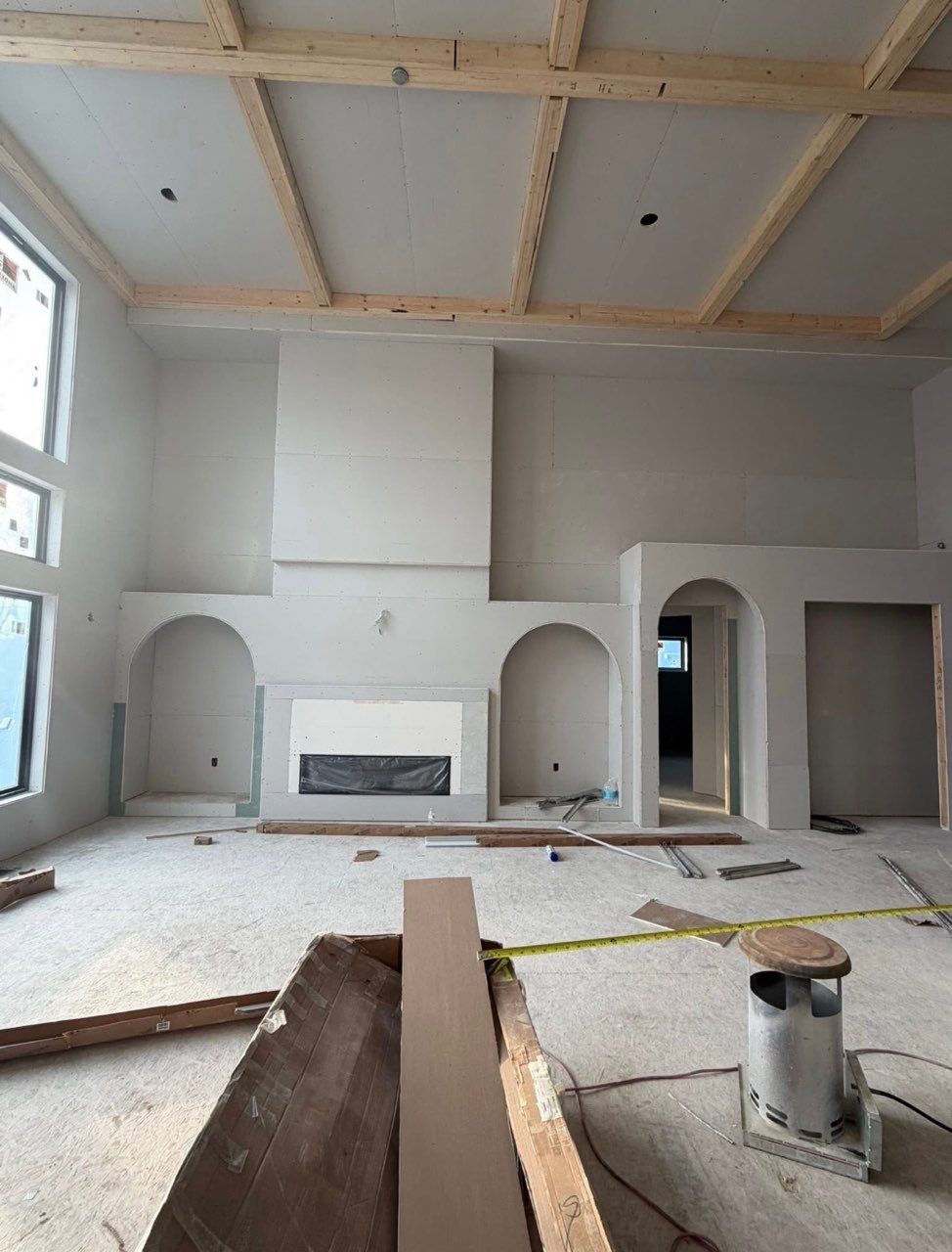 Unfinished living room with white fireplace, arched doorways, exposed ceiling beams, and construction materials on the floor.
