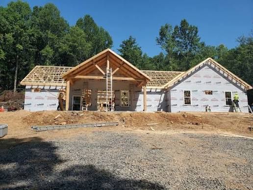 Partially built house with exposed wooden framing and white exterior walls under a clear blue sky