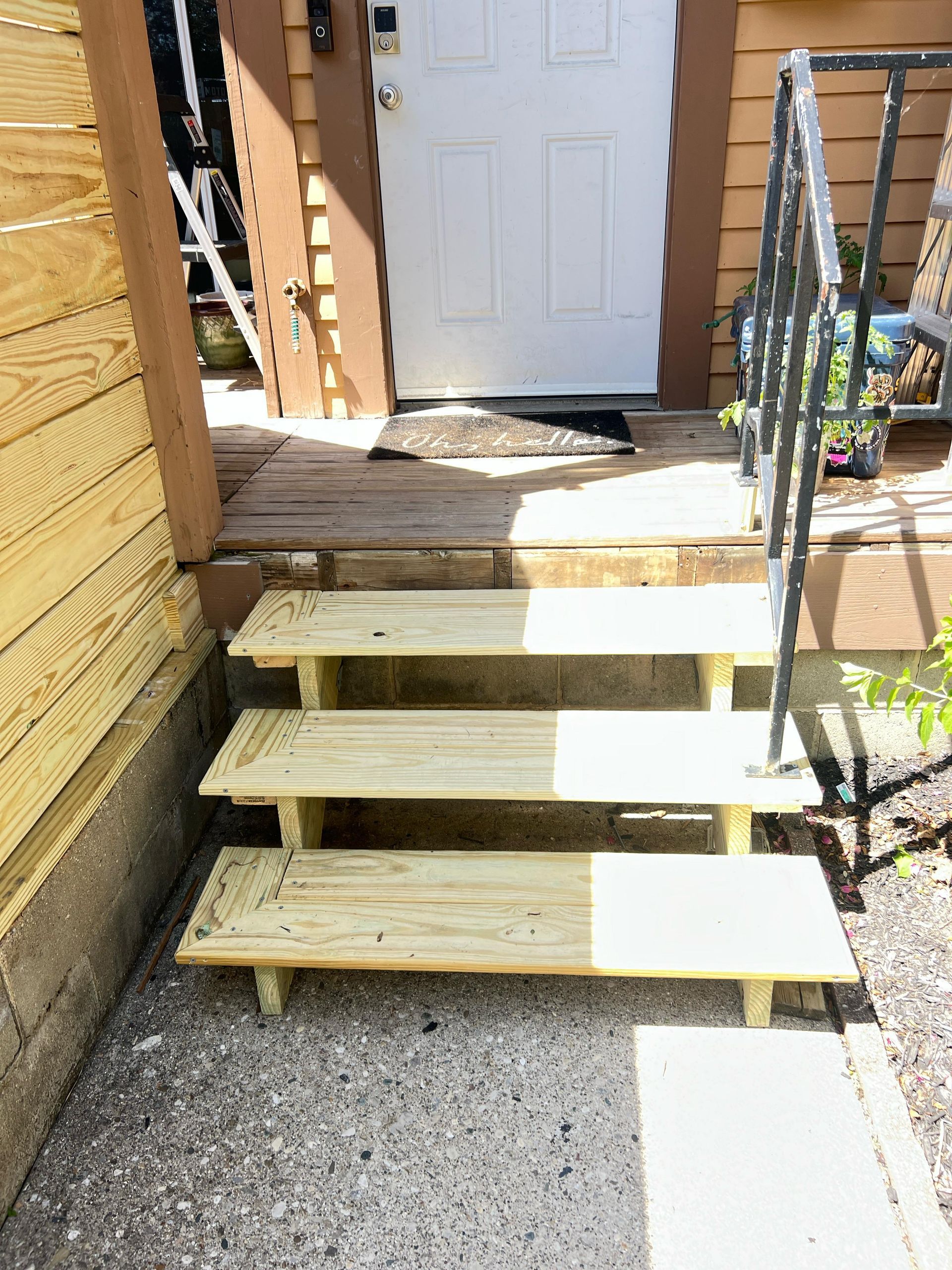 Wooden stairs with no front railing leading to a white door beside a yellow house and gravel walkway.