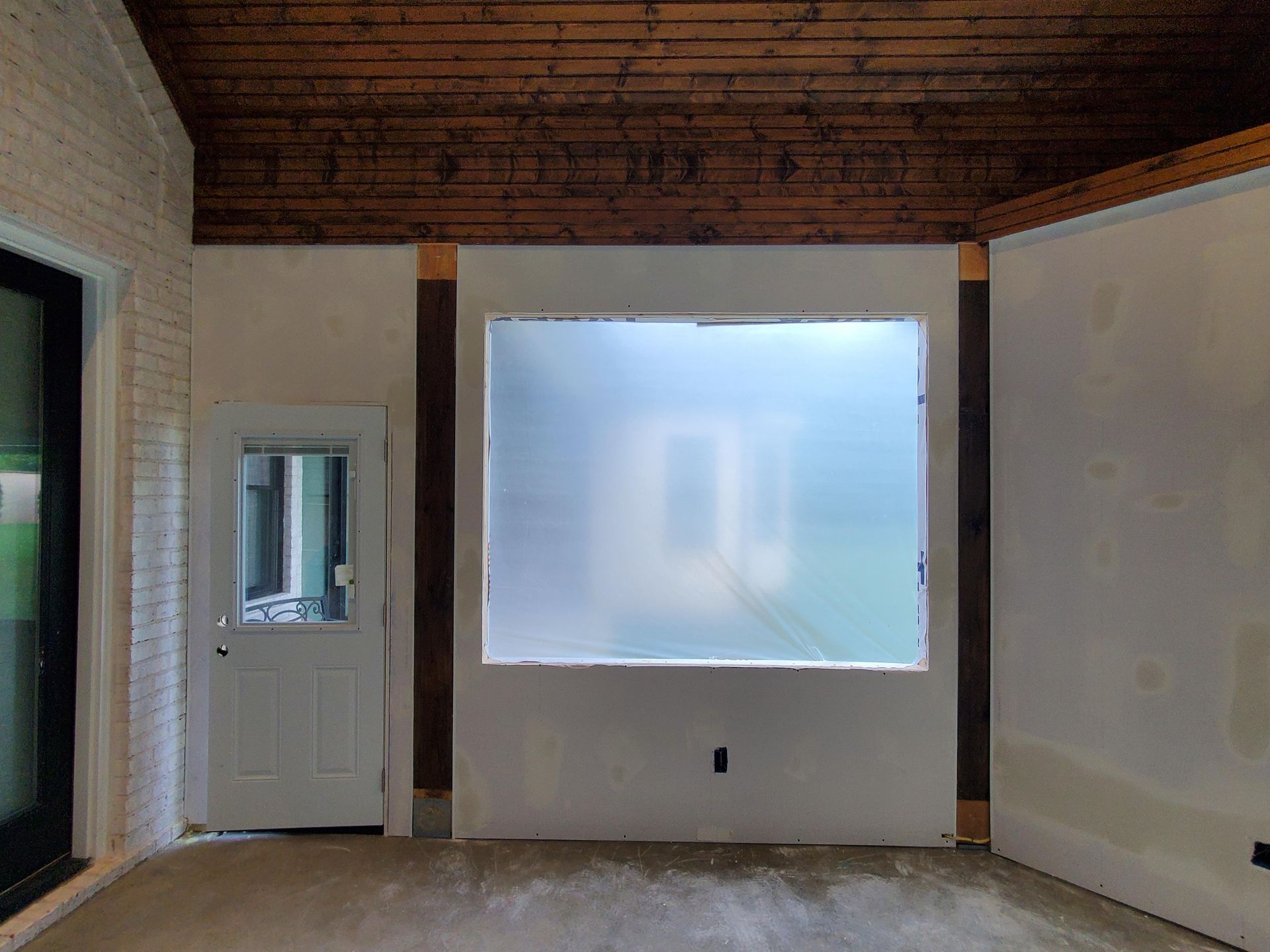 Empty room with unfinished walls, wood ceiling, and a large frosted window.