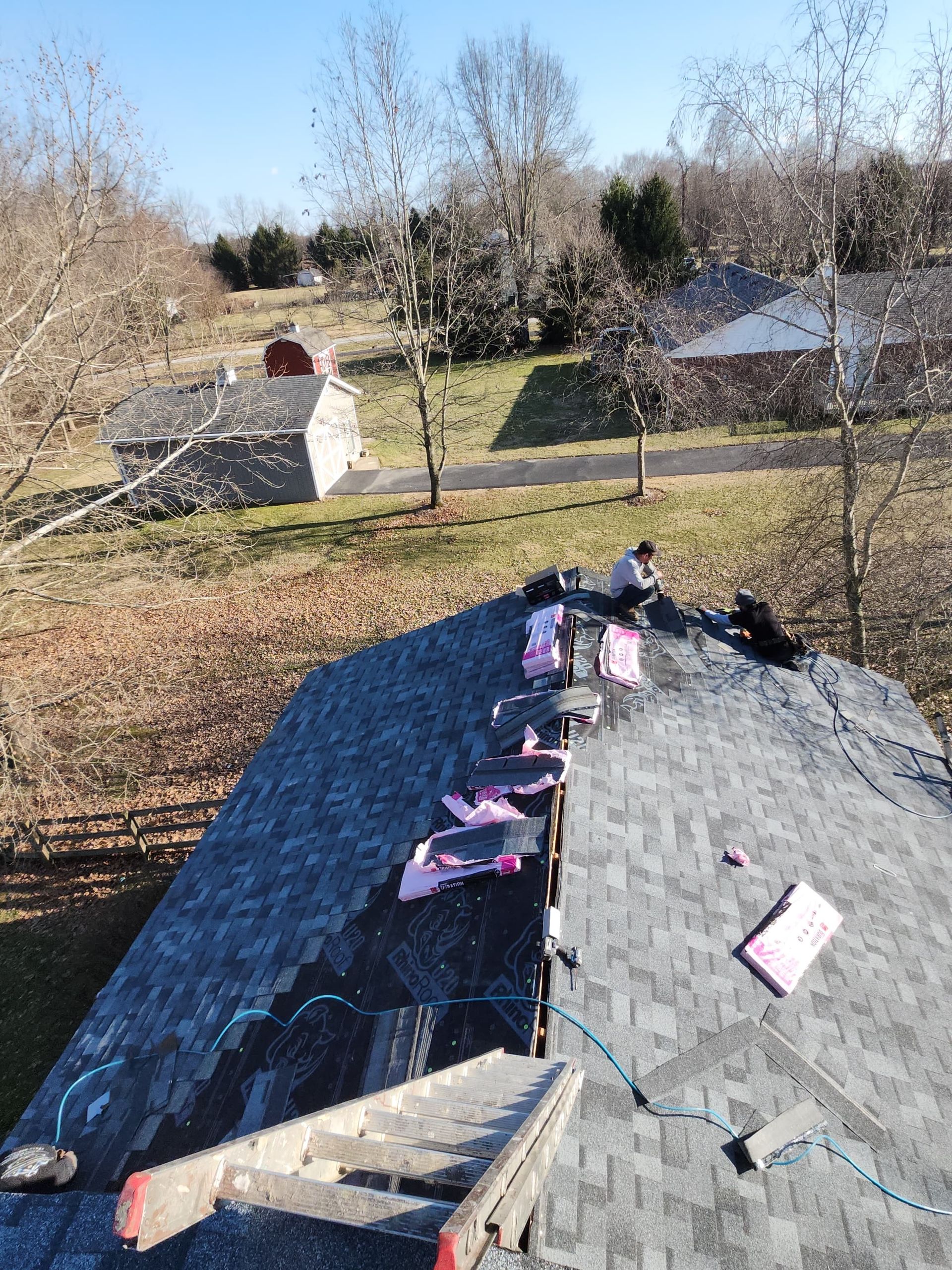 Rooftop with scattered materials in a grassy yard, with trees and small buildings in the background.