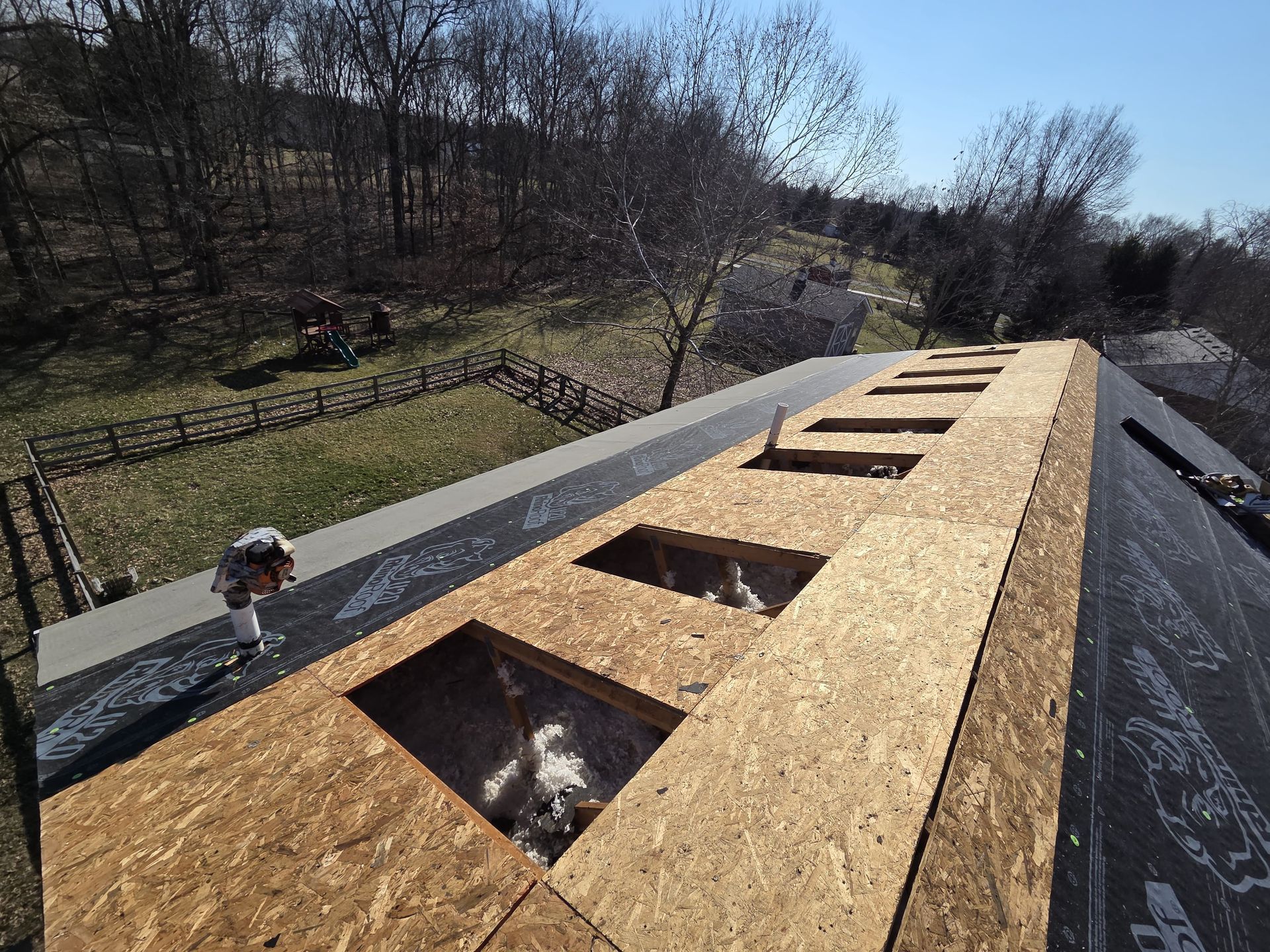 Roof under construction with OSB sheathing and skylight openings on a sloped hillside house
