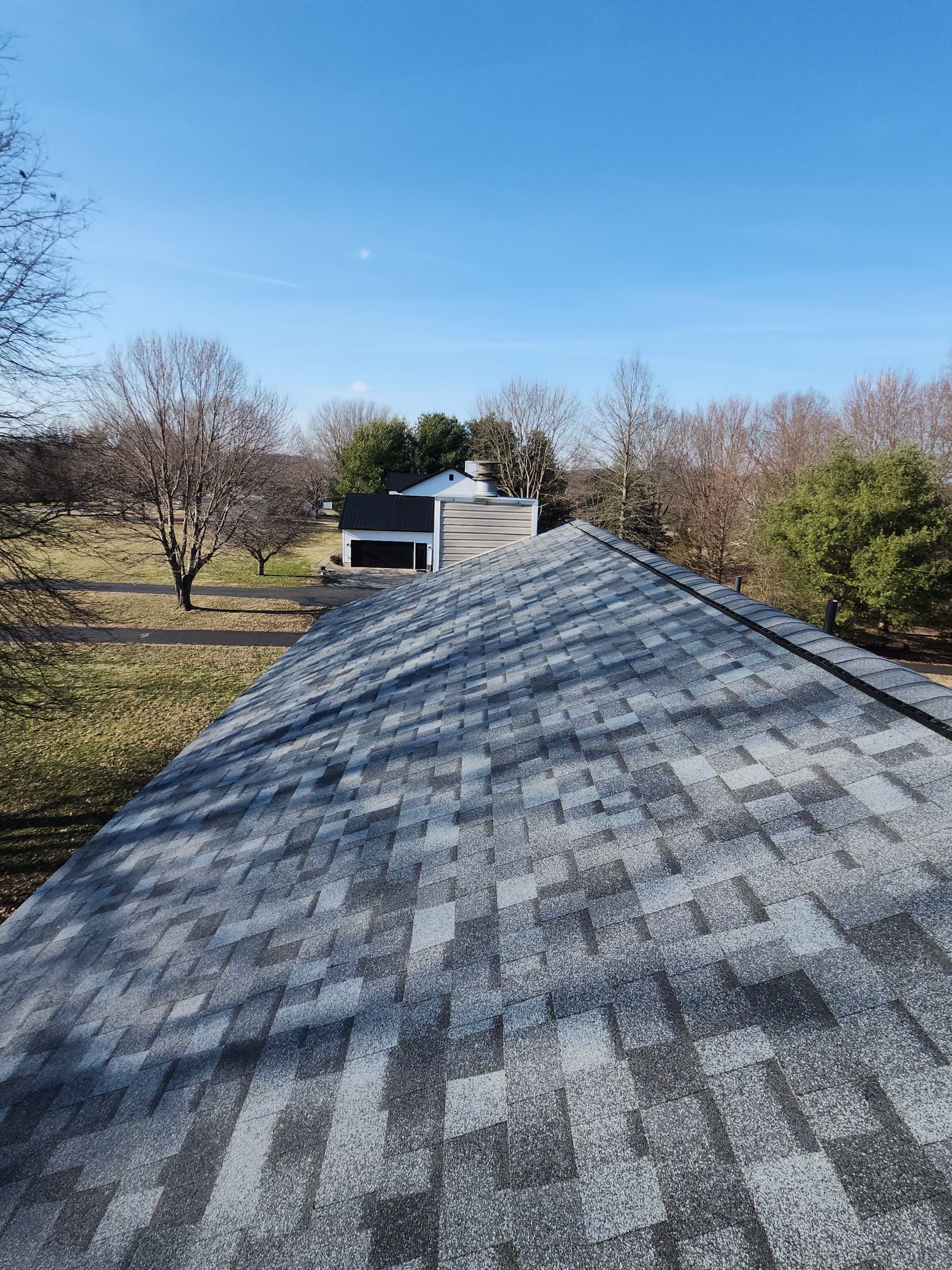 Roof shingles leading to a small white house surrounded by autumn trees under a blue sky