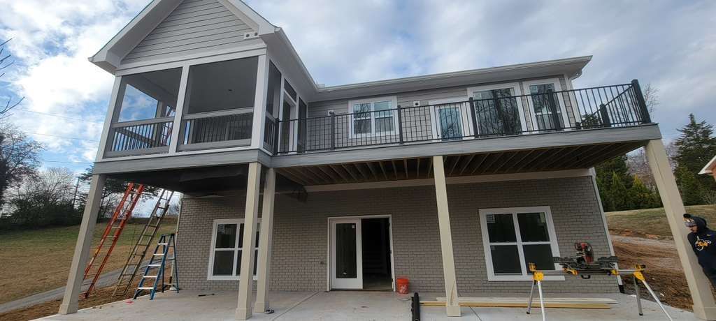Partially built two-story house with gray siding, front porch, and exposed framing under construction