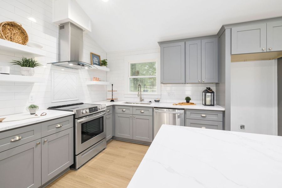 Bright modern kitchen with gray cabinets, white countertops, stainless stove, and wood floor.