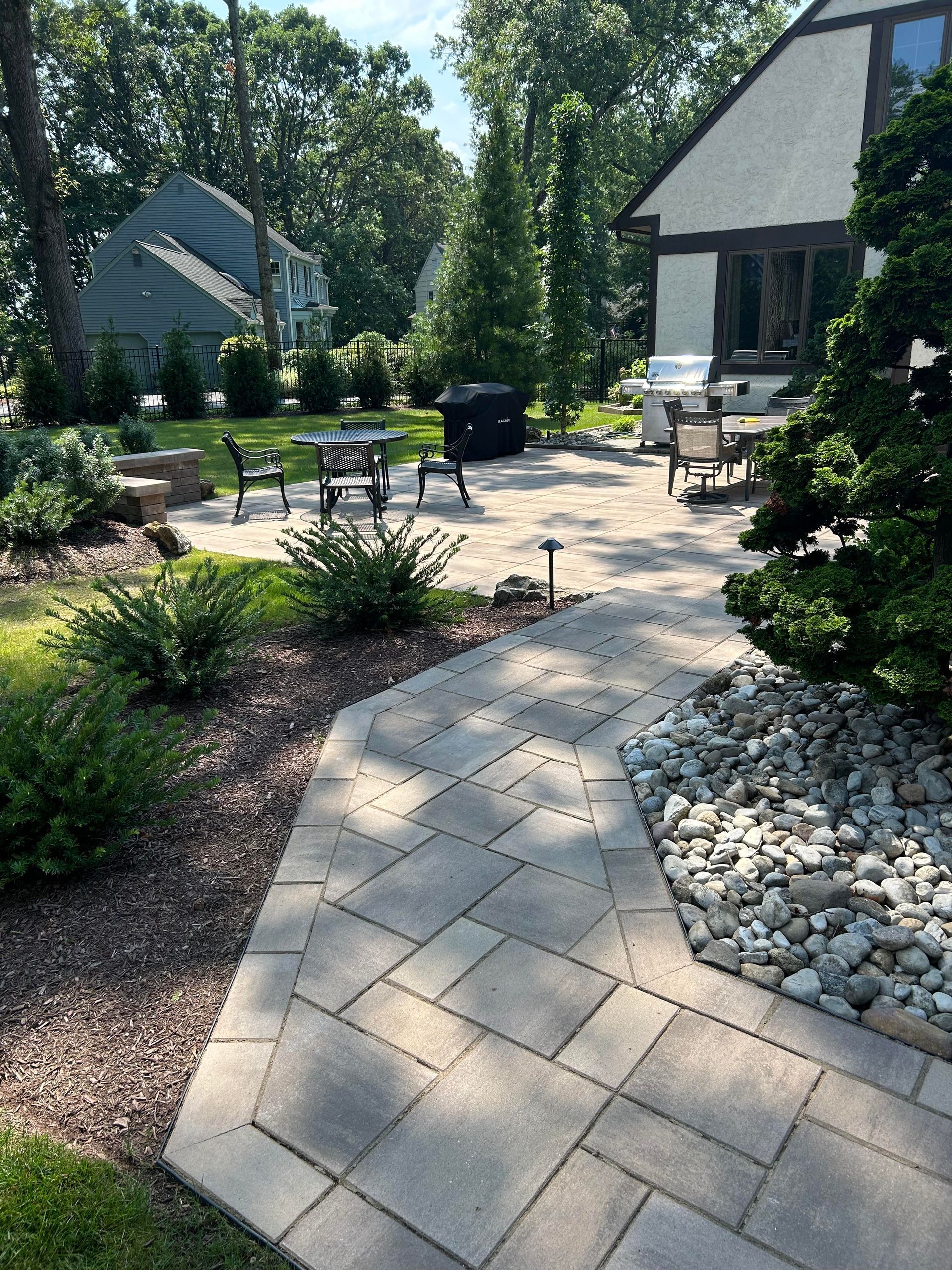 Stone patio garden path with outdoor seating, shrubs, and white gravel beside a house