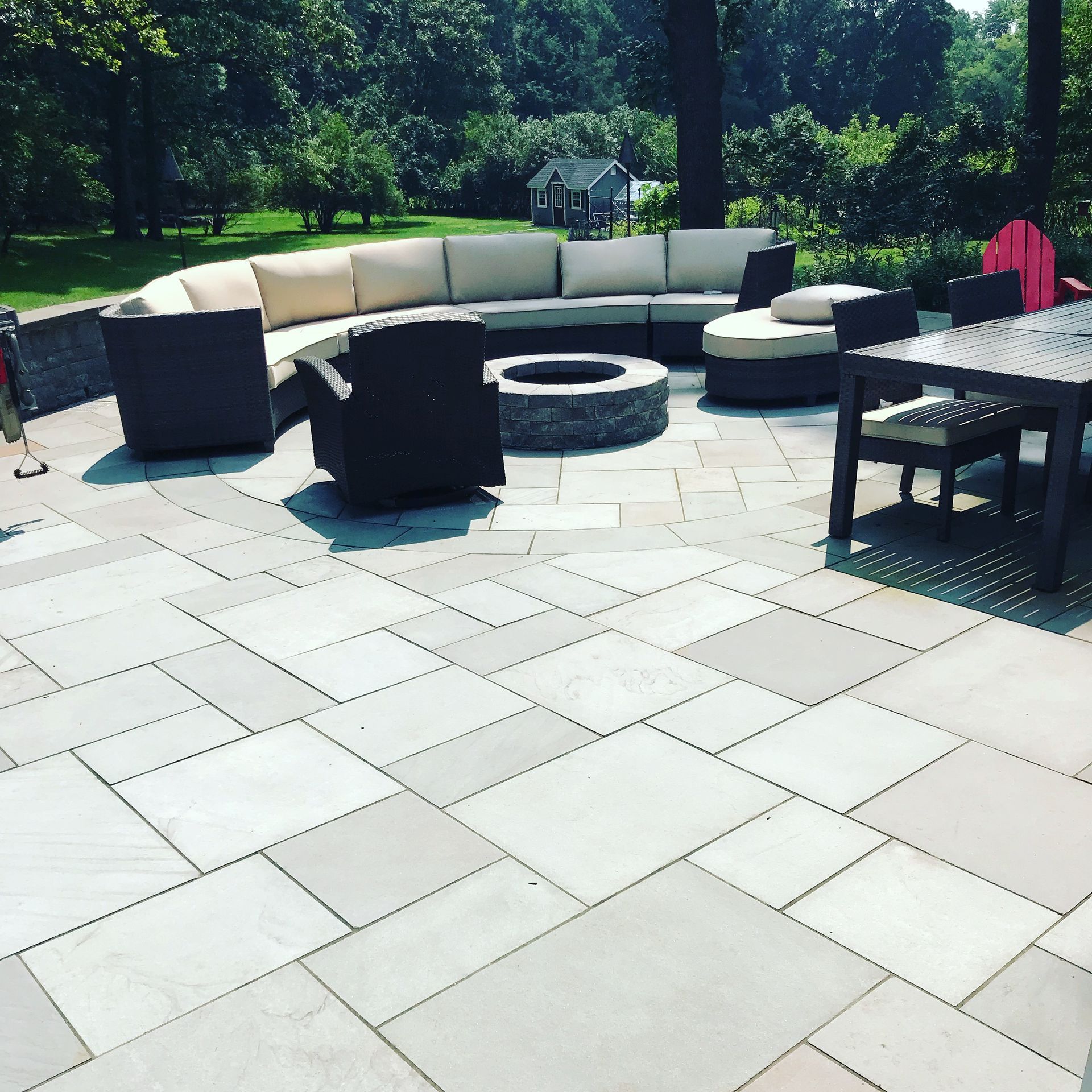 Modern backyard patio with curved outdoor sofa, fire pit, and dark chairs on light stone pavers