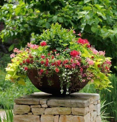 Flower-filled urn planter on a stone pedestal in a lush garden setting