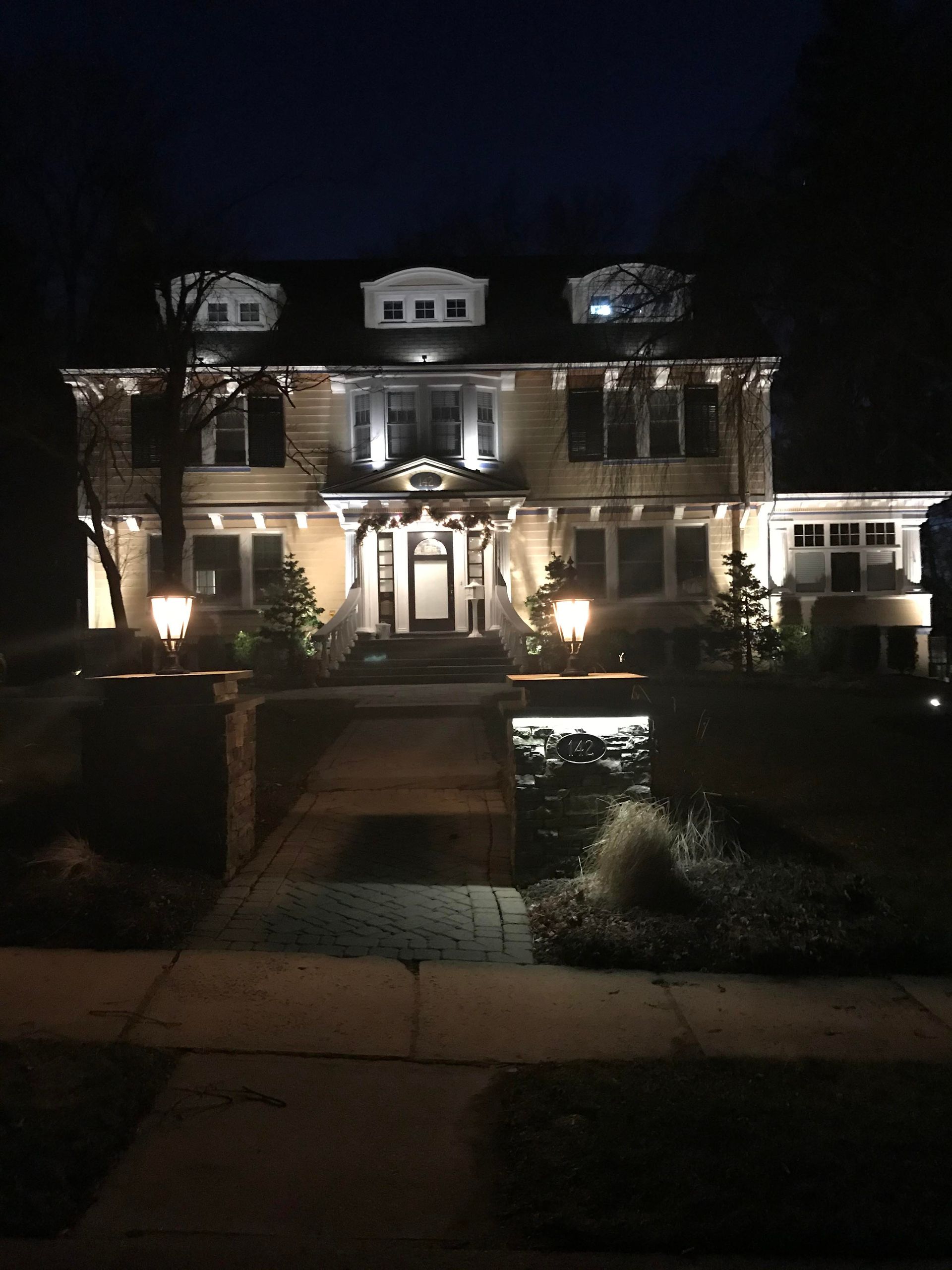 Illuminated two-story brick house at night with a front walkway and landscaped yard