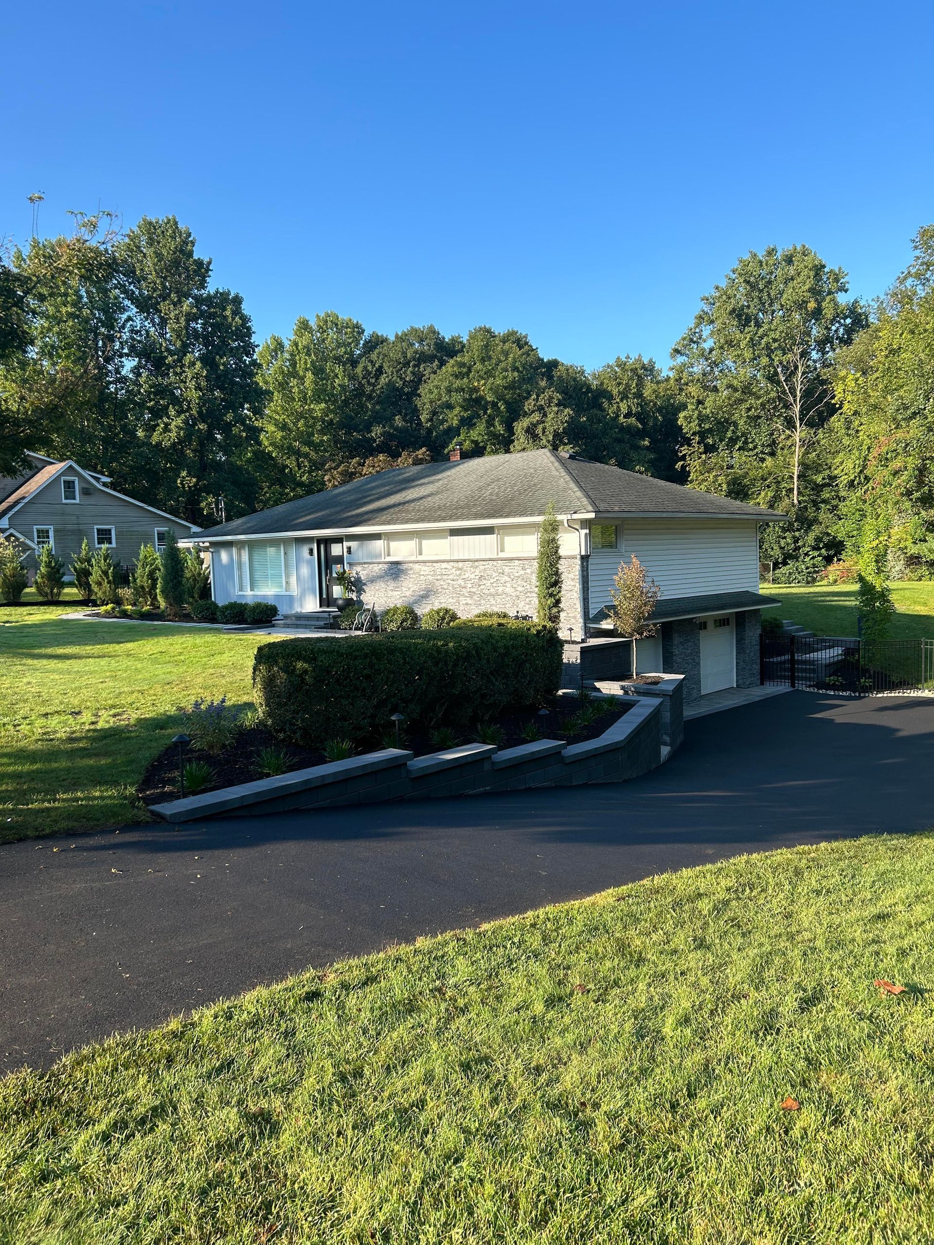 Small white house with a ramp and garage, set on a sunny suburban lawn with trees and blue sky.