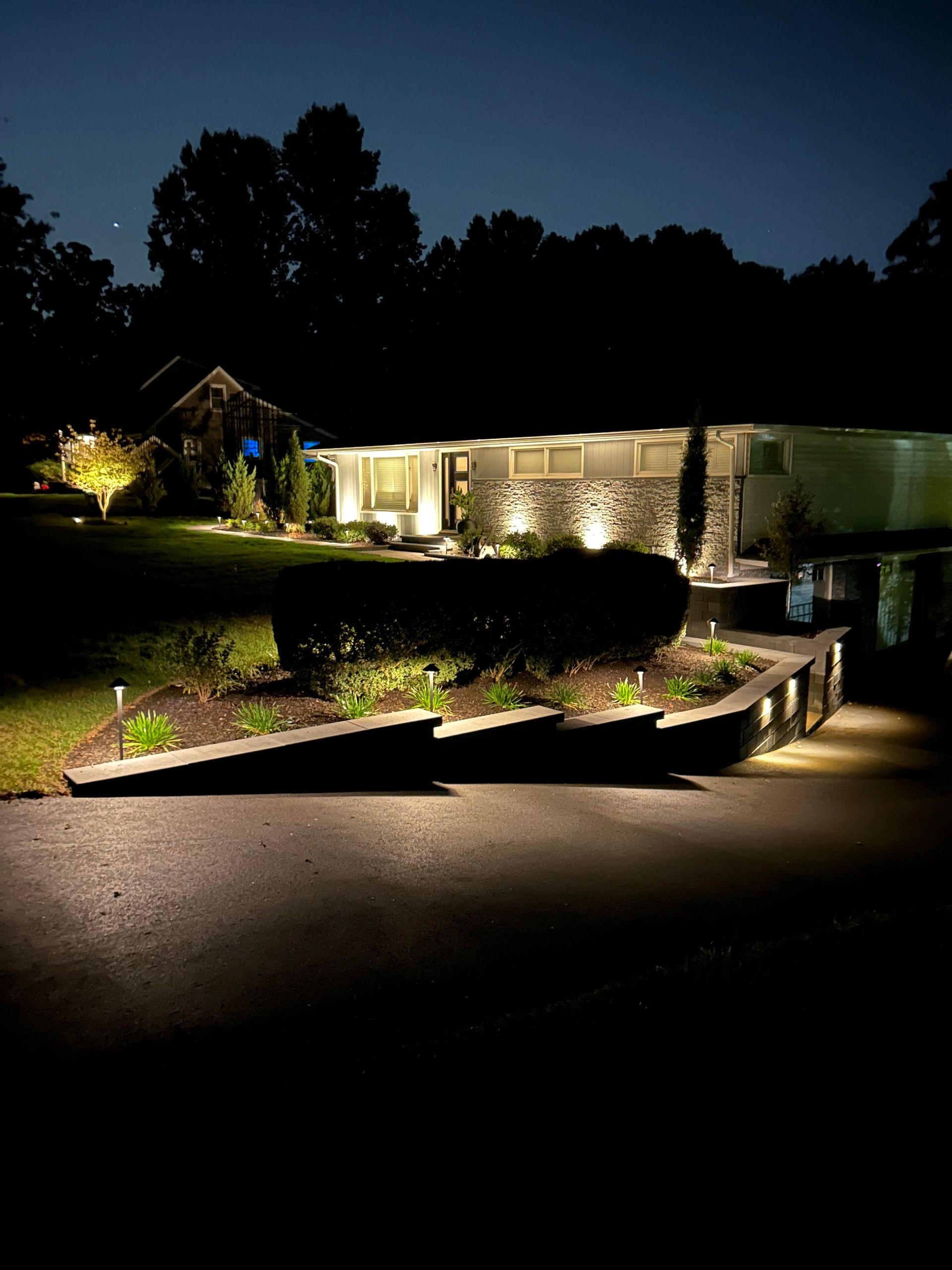 Nighttime view of a lit modern house with a landscaped driveway and dark trees in the background