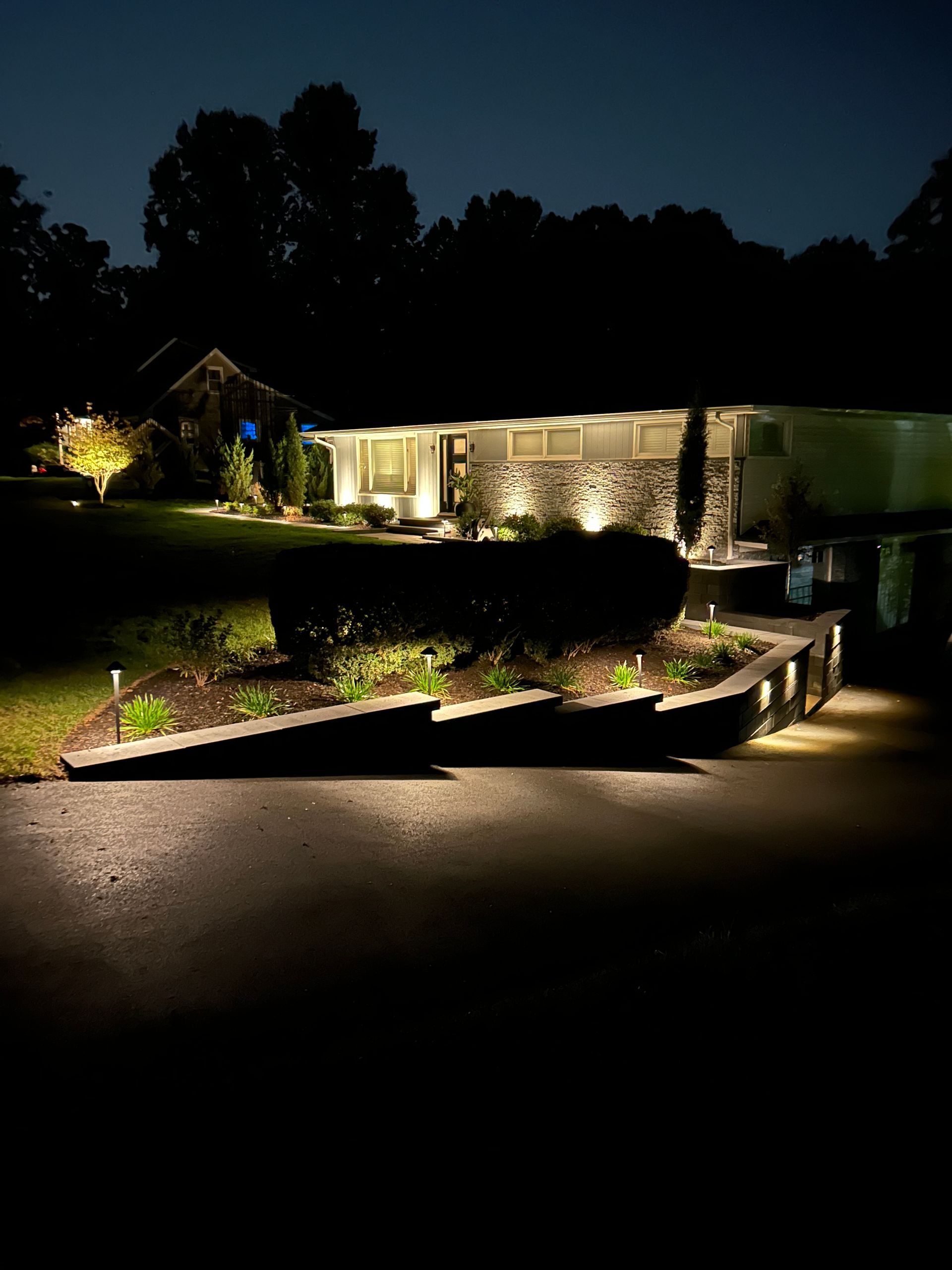 Lit suburban house and garden at night with illuminated driveway and landscape lighting