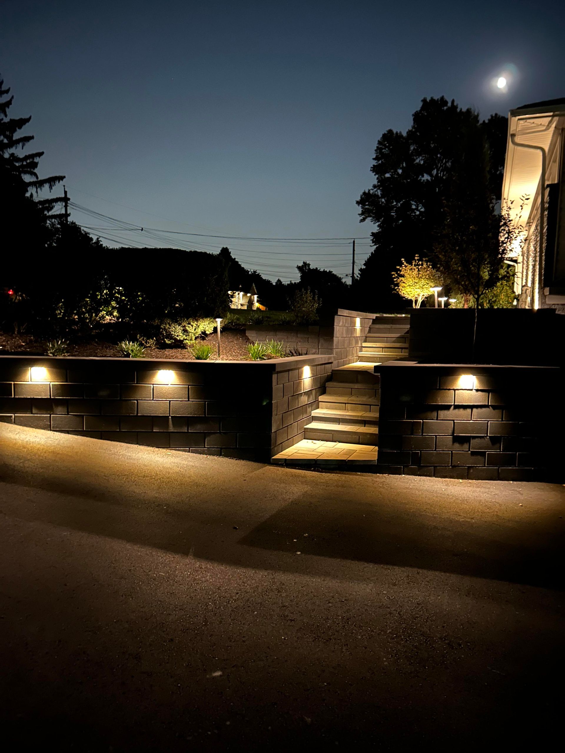 Nighttime view of a lit stone terrace and steps with a moonlit sky and trees in the background