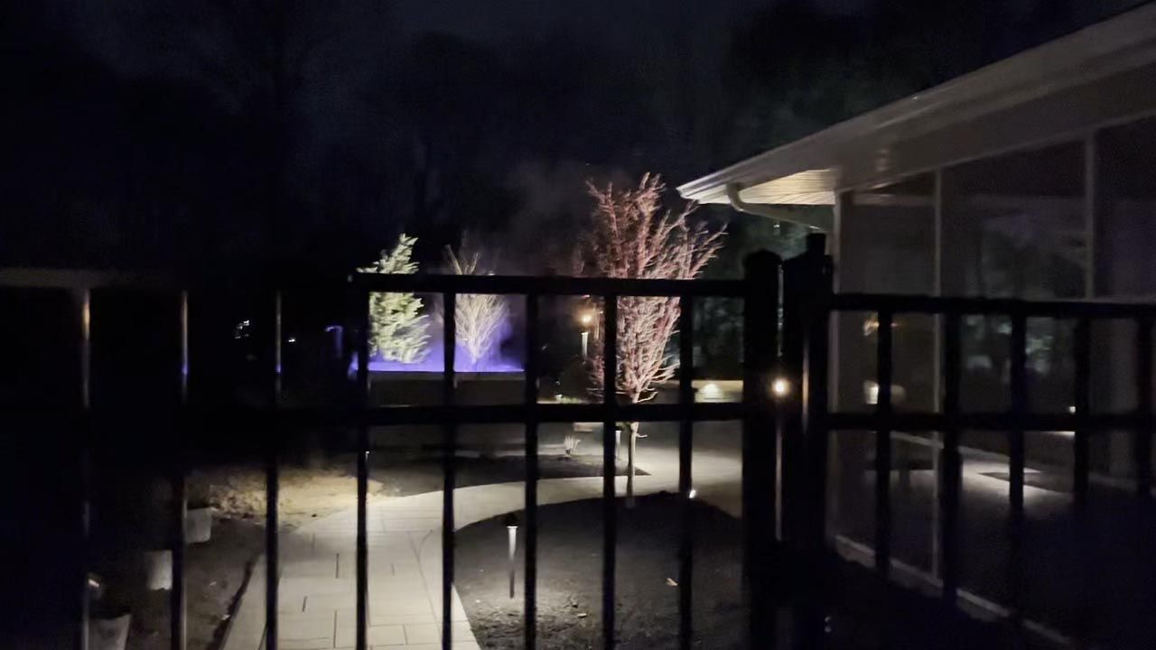 Nighttime view from a patio of a lit garden fountain behind a black railing
