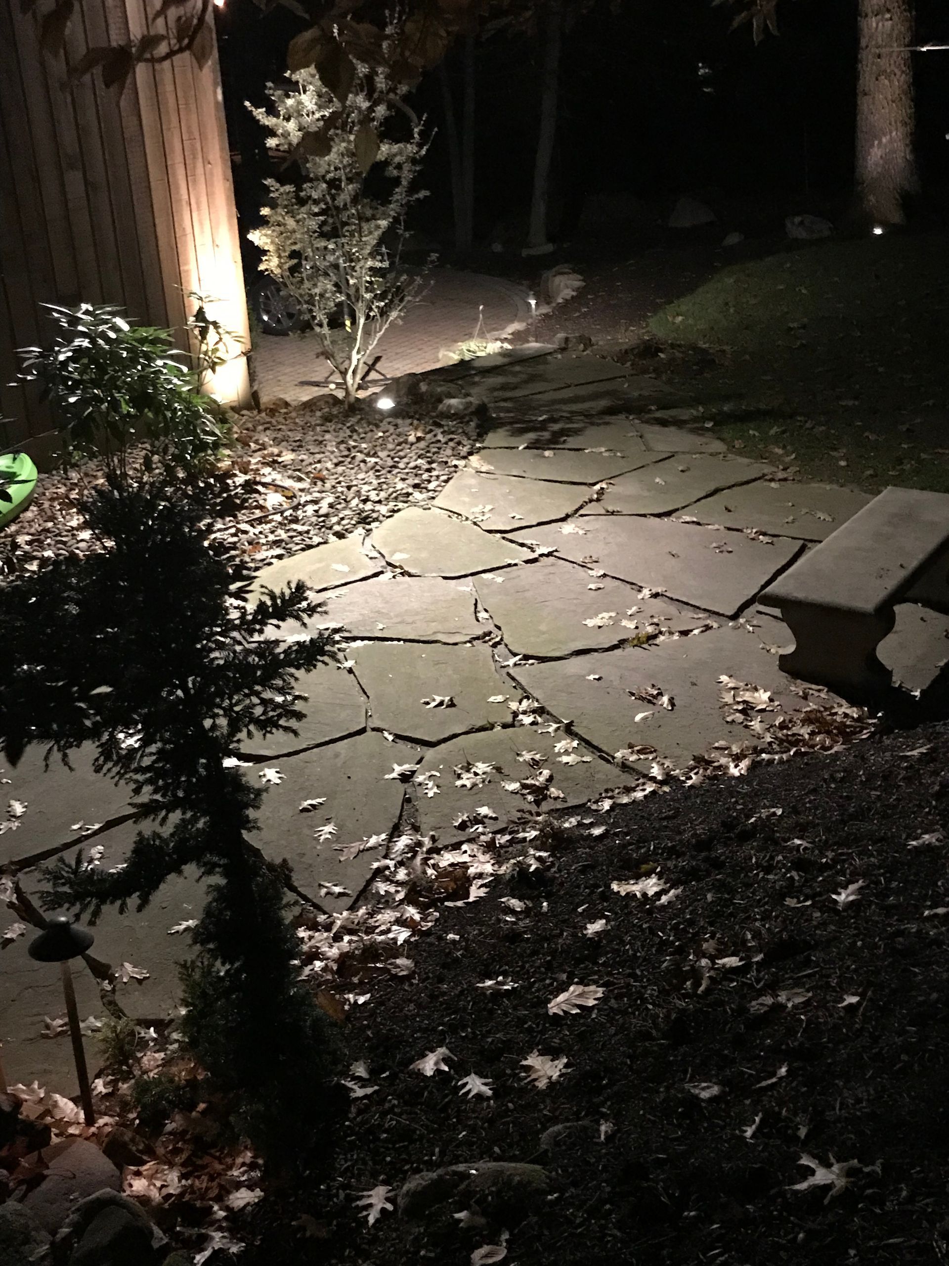 Dimly lit cracked stone patio with scattered leaves and a small bench at night