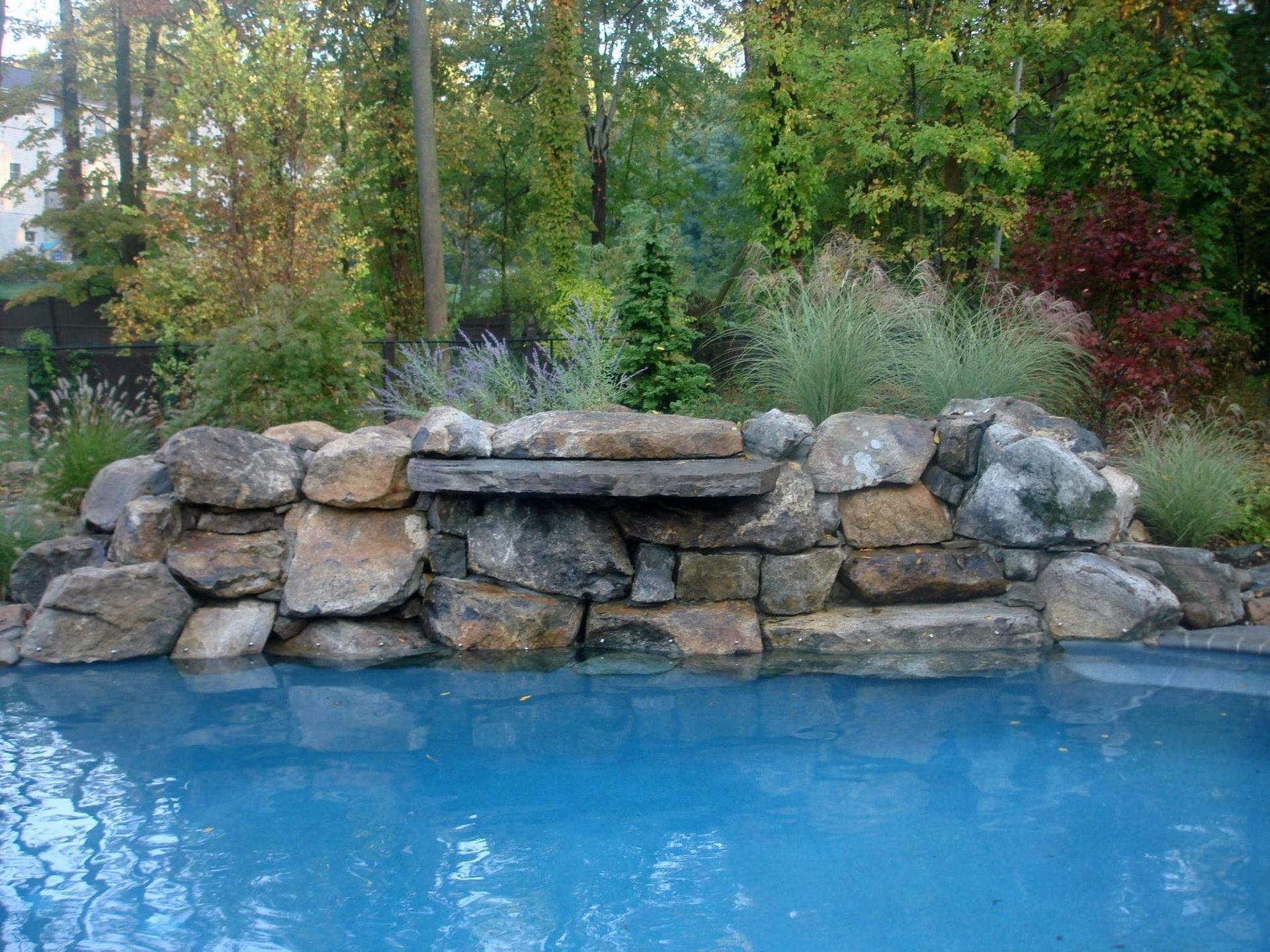 Stone waterfall feature beside a blue pool, surrounded by lush greenery