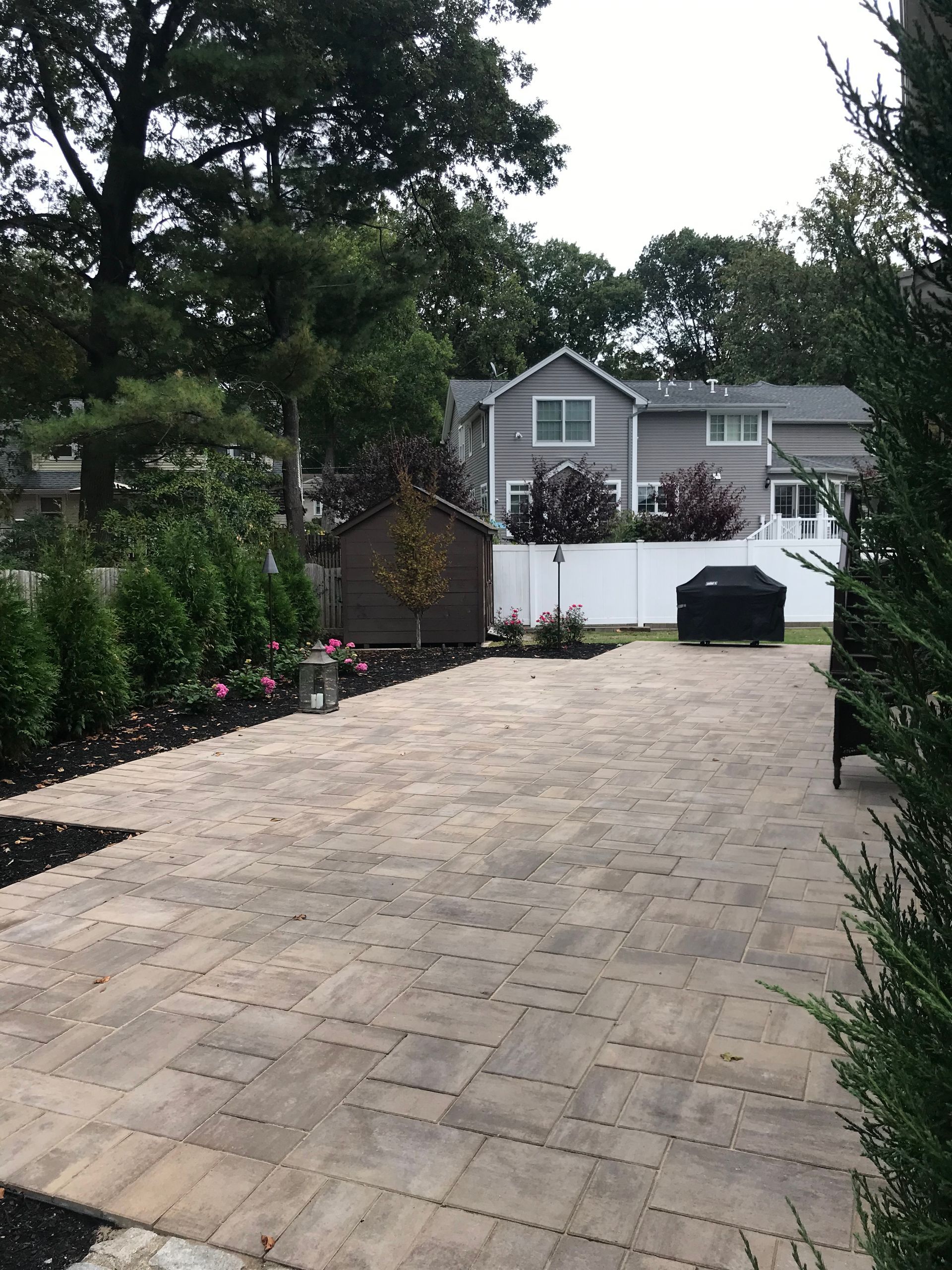Long brick driveway leading to a house with white fence and greenery on both sides