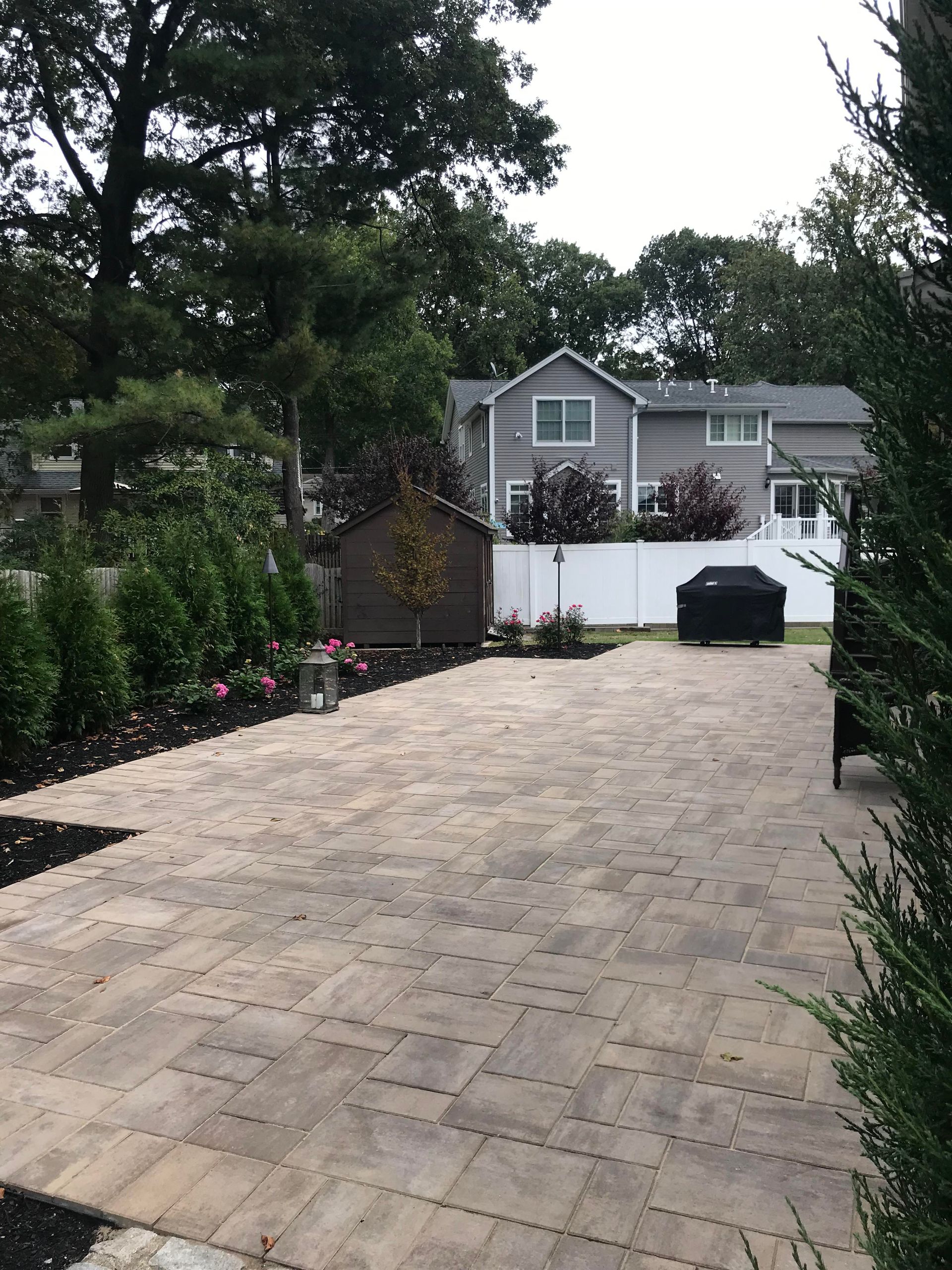 Paved driveway leading to a house with a white fence and shrubs on both sides